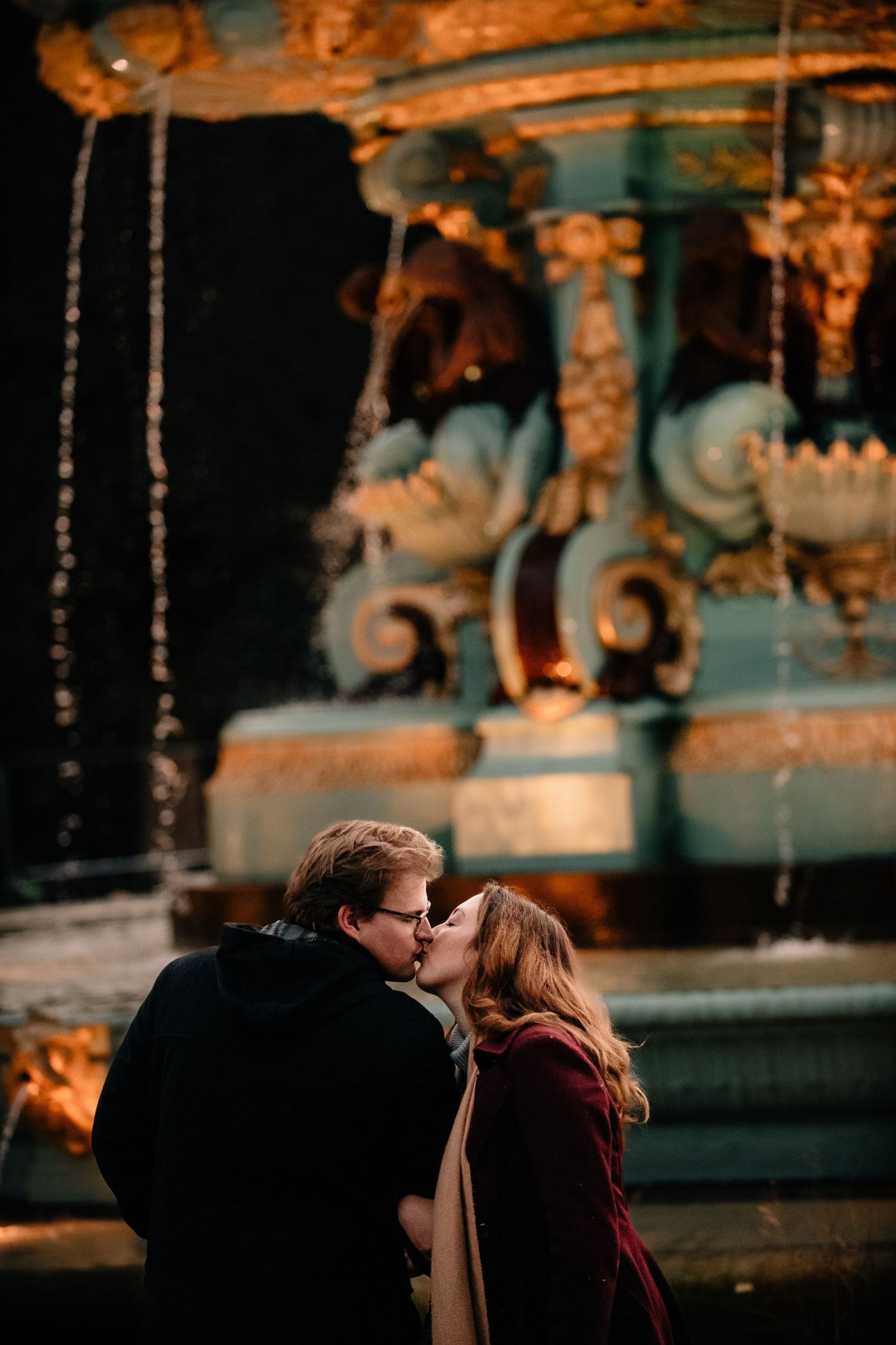 A romantic couple shares a passionate kiss at sunset with warm golden light filtering through trees in the background.