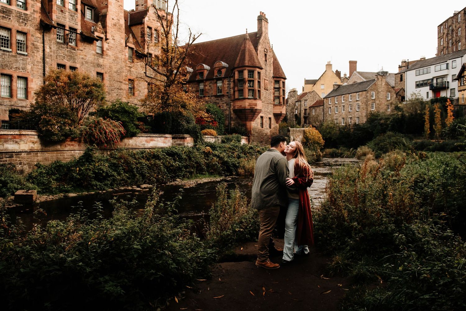 A couple stands on a path surrounded by historic architecture in Edinburgh's old town.