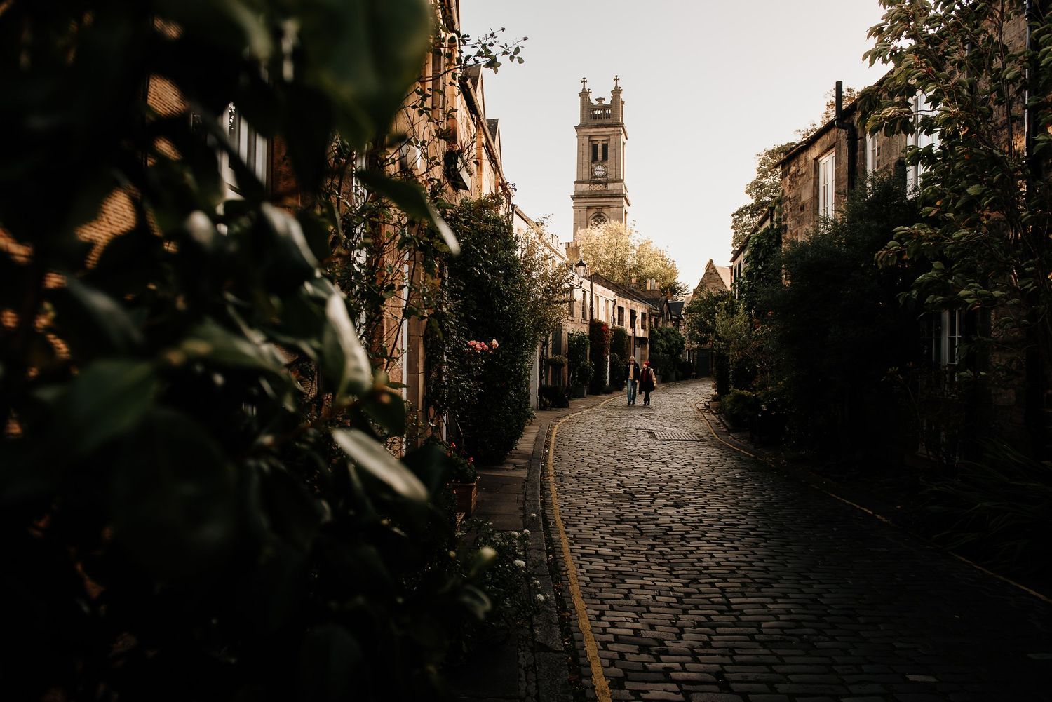 Atmospheric view of a narrow cobblestone lane with historic buildings and church spire.