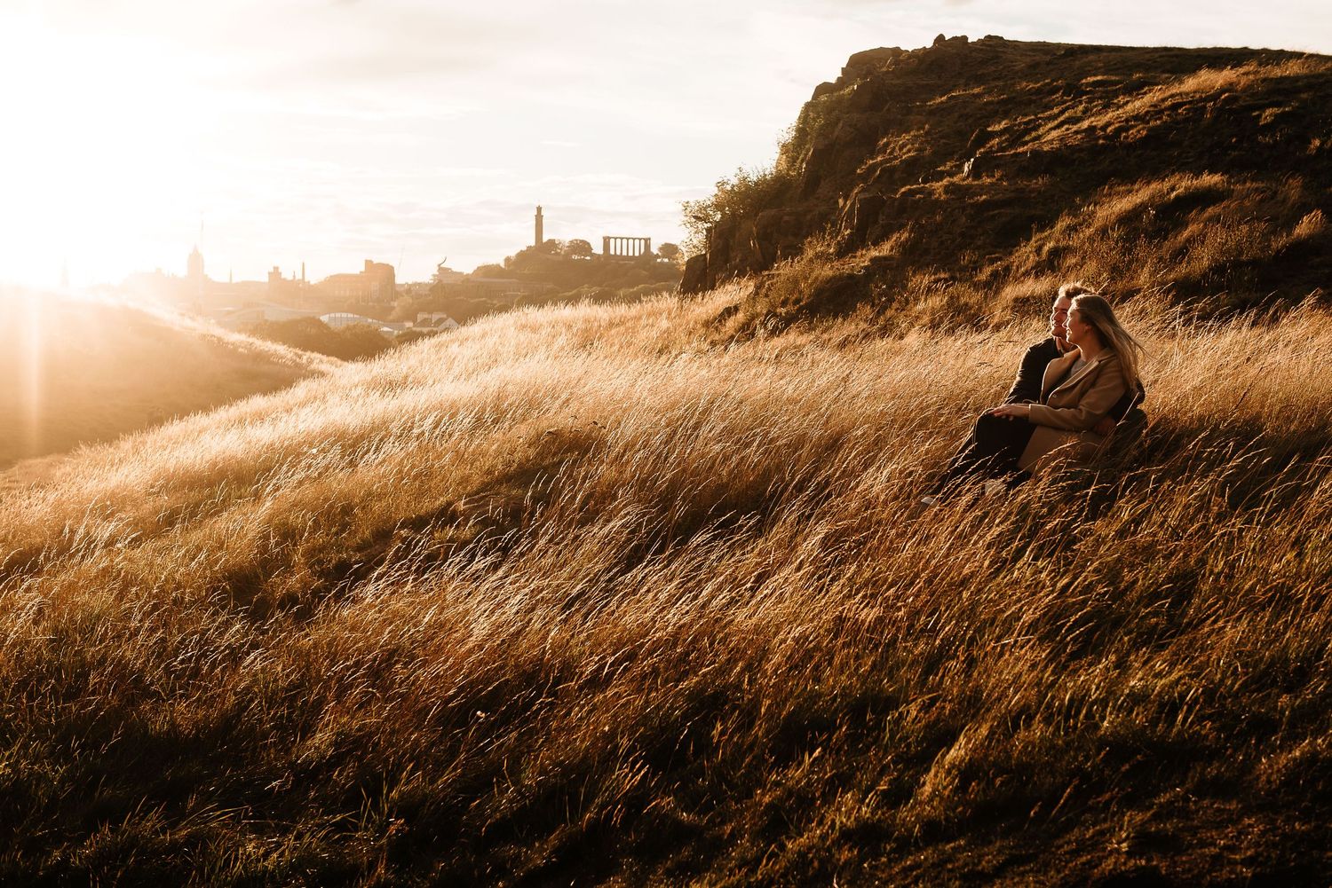 Warm sunlight illuminates rolling hills and dry grass on a mountainside trail.