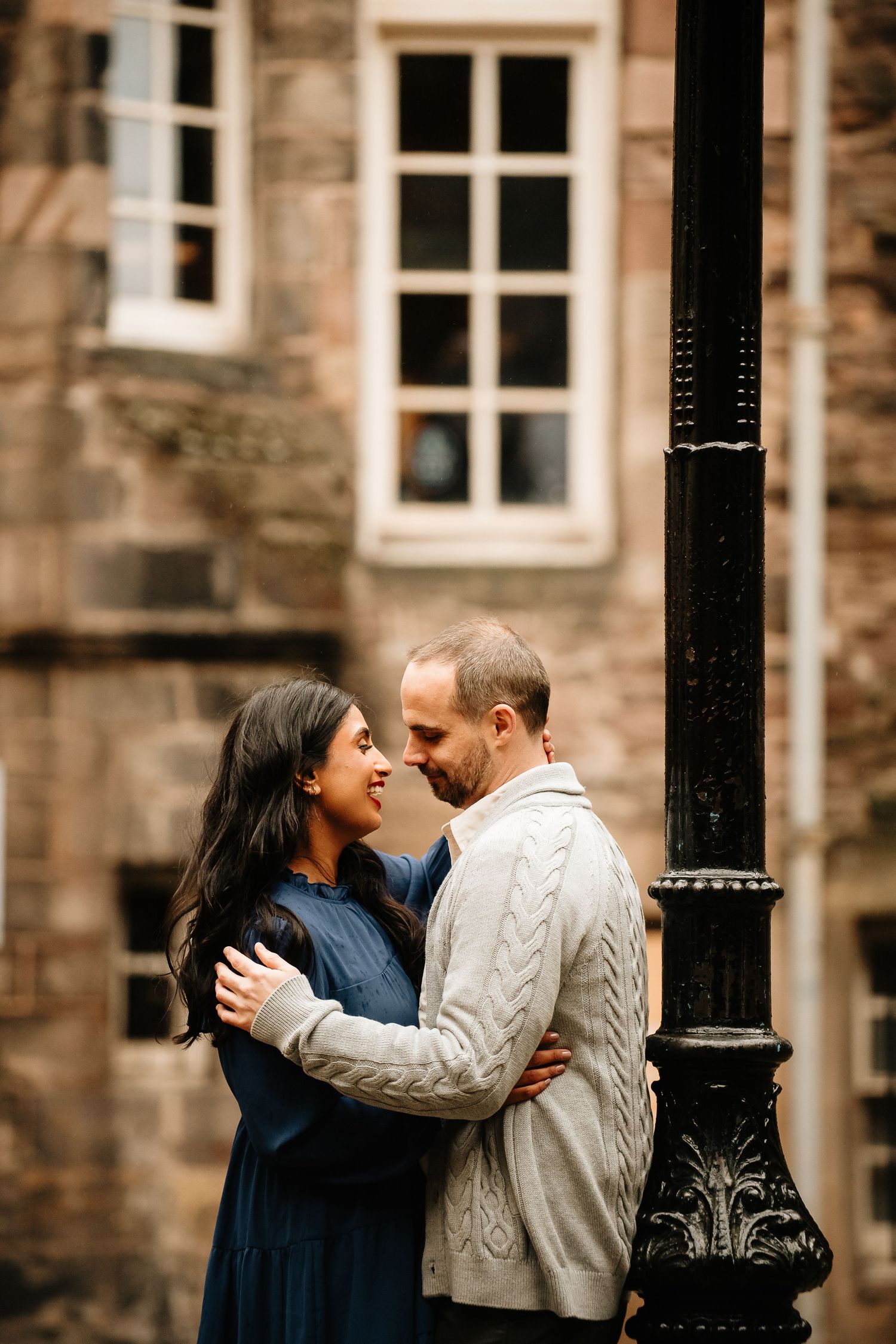 A couple shares an intimate moment while embracing against a stone building with ornate architecture in the background.