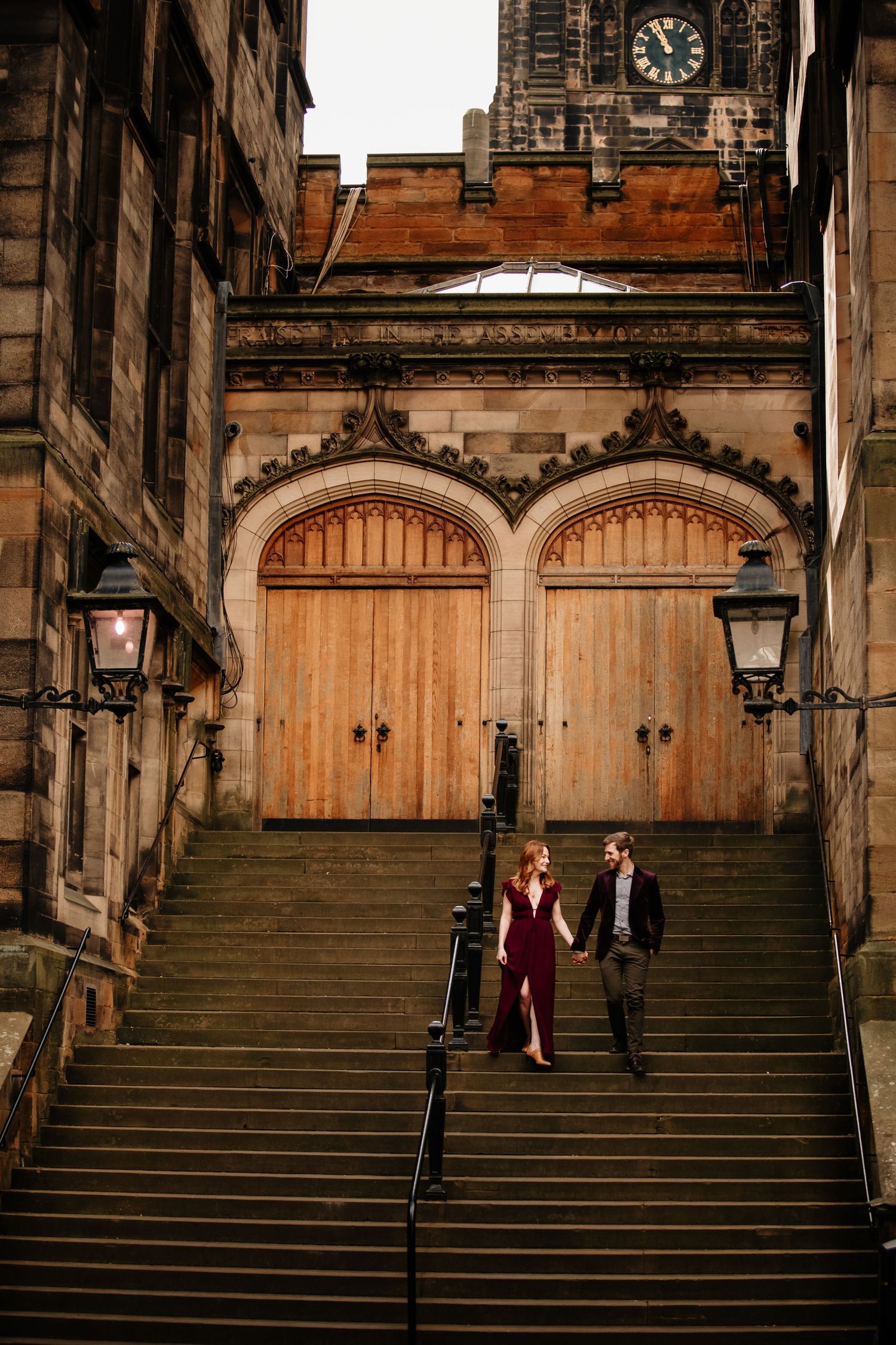 A couple poses on historic stone steps in Edinburgh with wooden doors and stone architecture in the background.