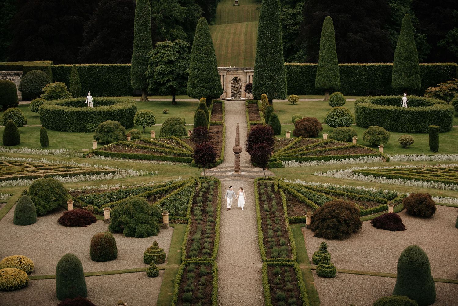 Formal garden with symmetrical hedges and manicured pathways leading to a grand estate.