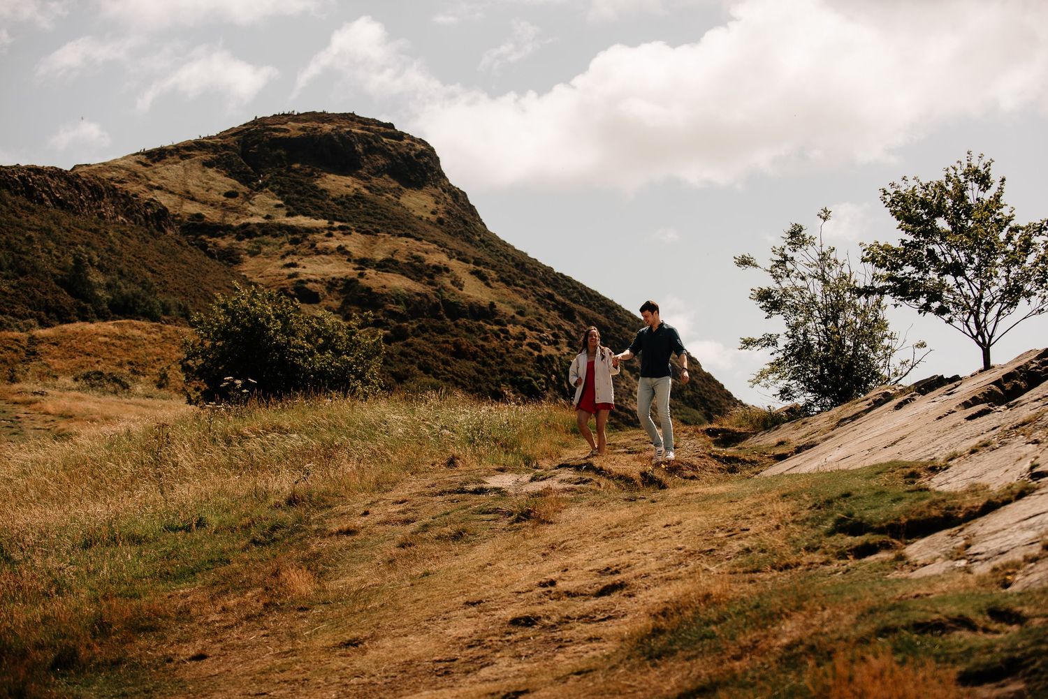 Two people hiking along a rugged mountain trail with dramatic cloudy skies.
