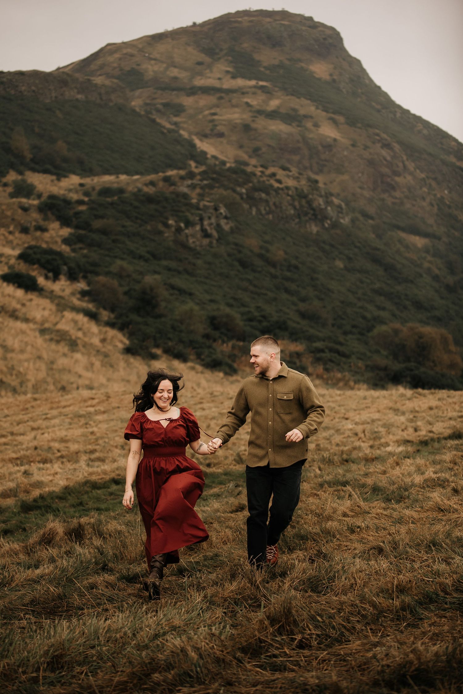 Couple sharing a romantic moment on a hillside with dramatic mountain landscape in the background.