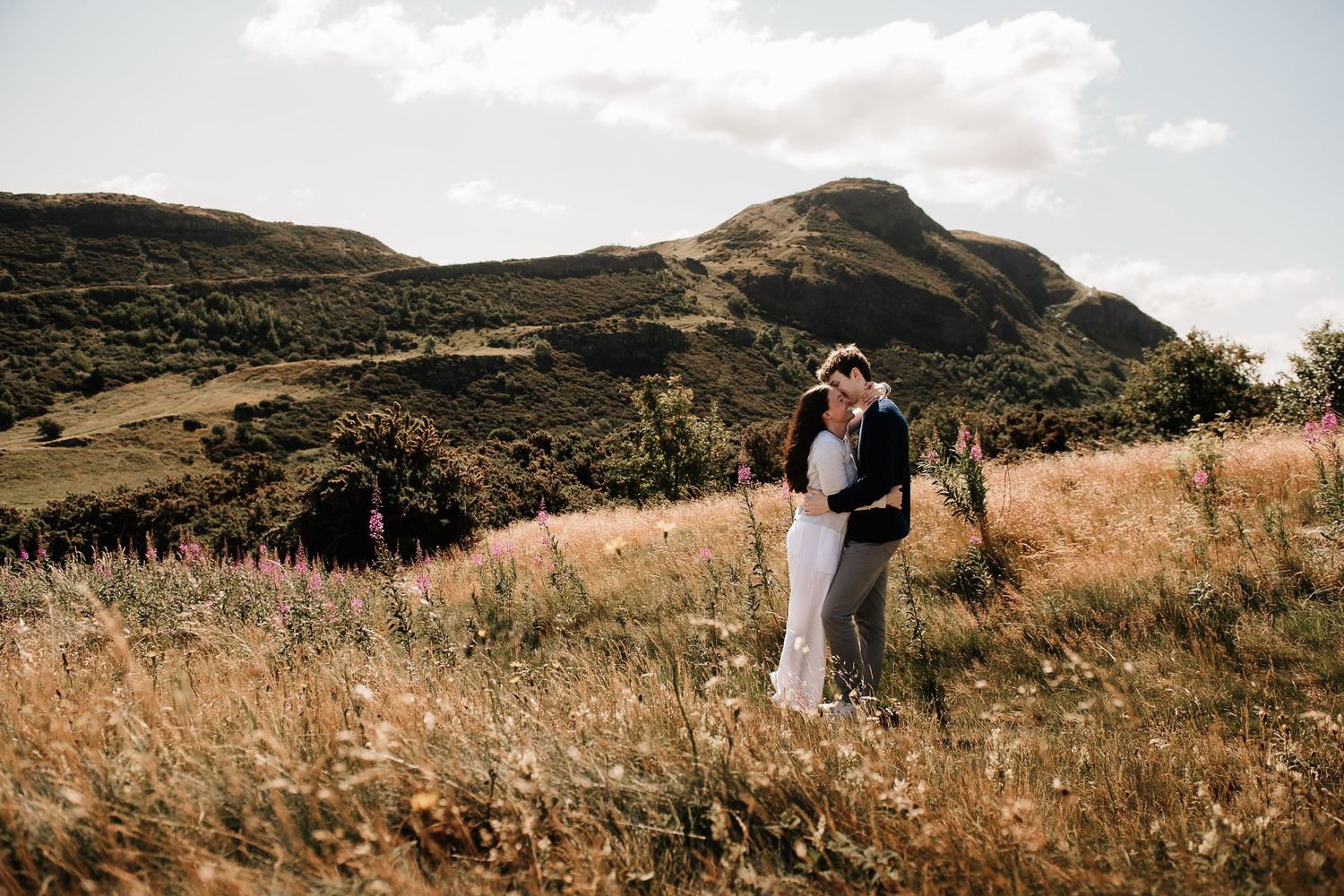 A couple stands together on a scenic hilltop overlooking a dramatic landscape.