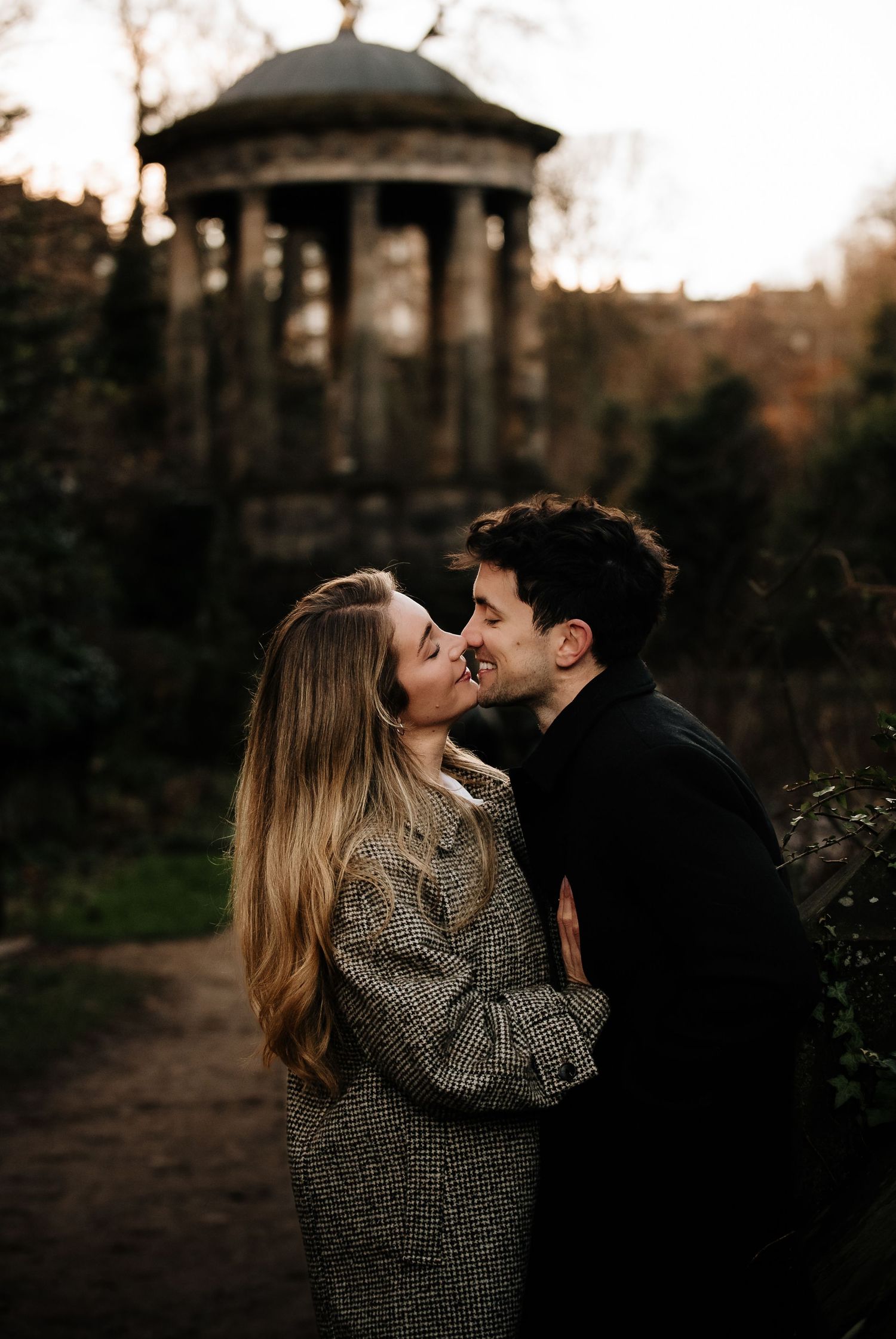 A romantic moment captured at sunset near a gazebo in a garden setting.