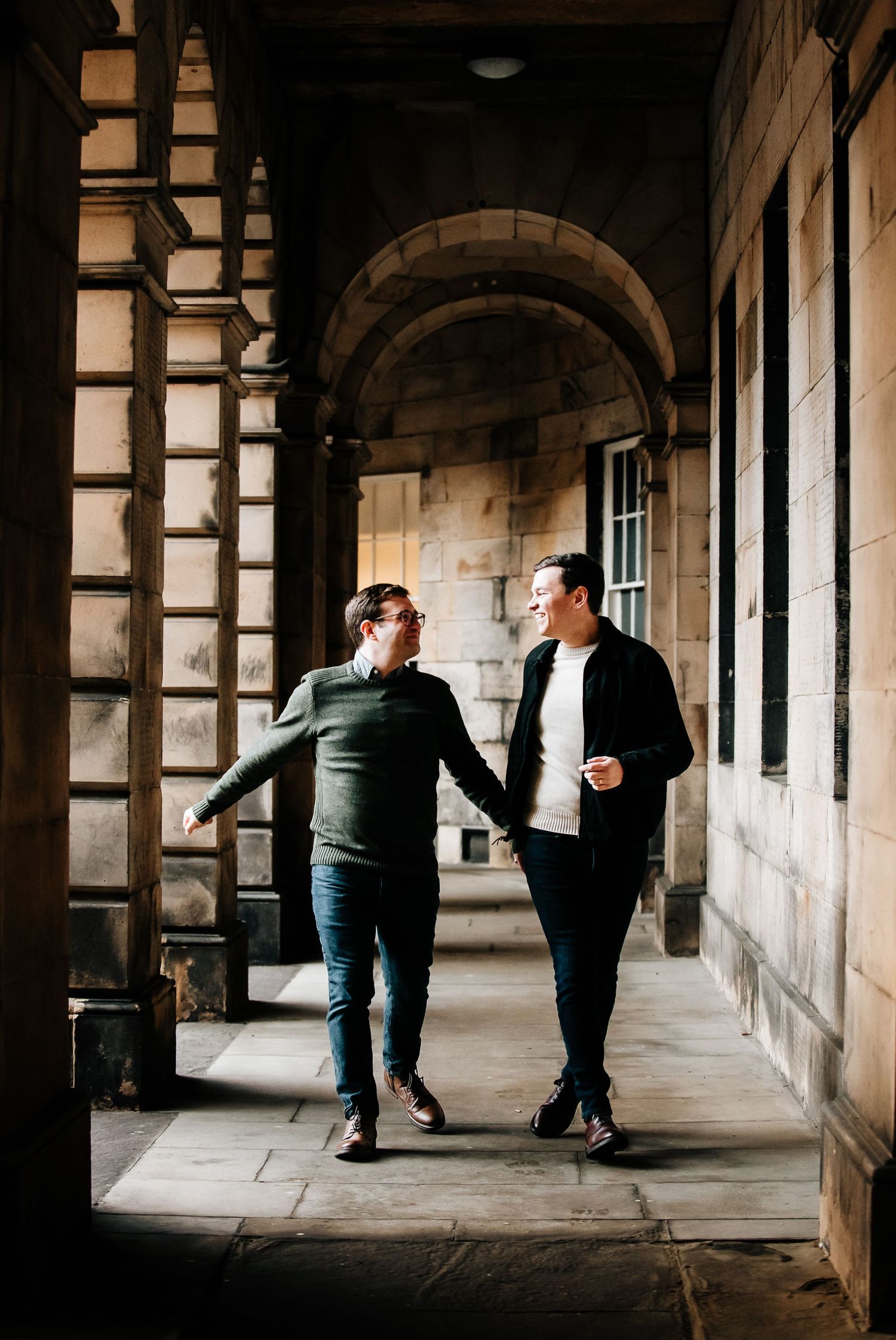 Couple dancing playfully in historic stone colonnade with dramatic lighting.