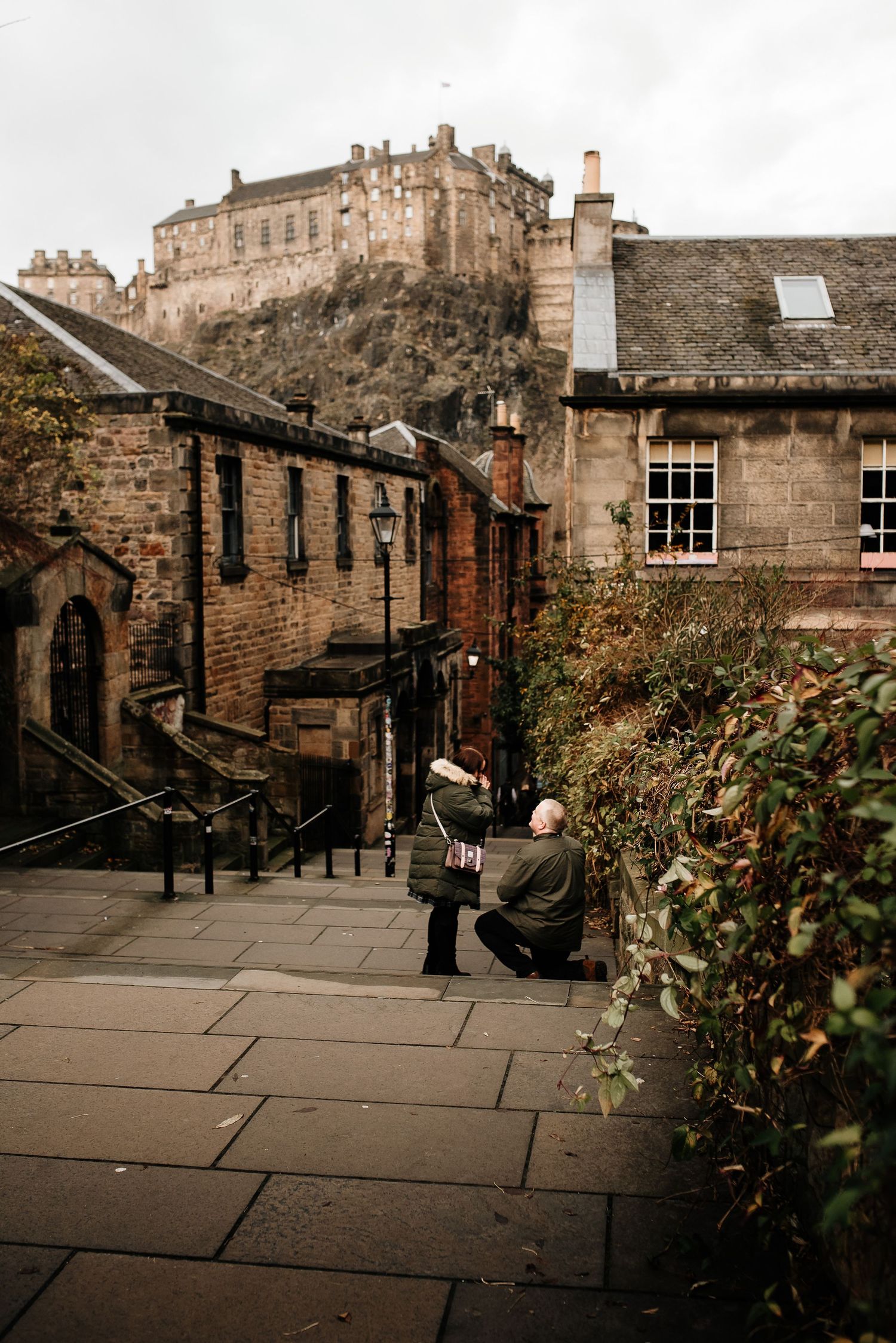 Historic cobblestone pathway with stone buildings and Edinburgh Castle visible in the background at sunset.