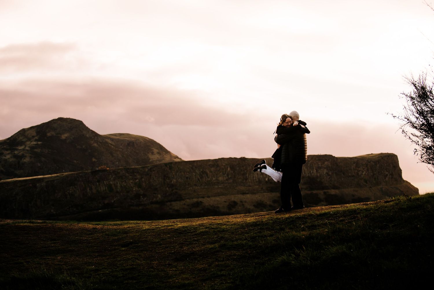 A silhouetted embrace against a dramatic mountain landscape at sunset.