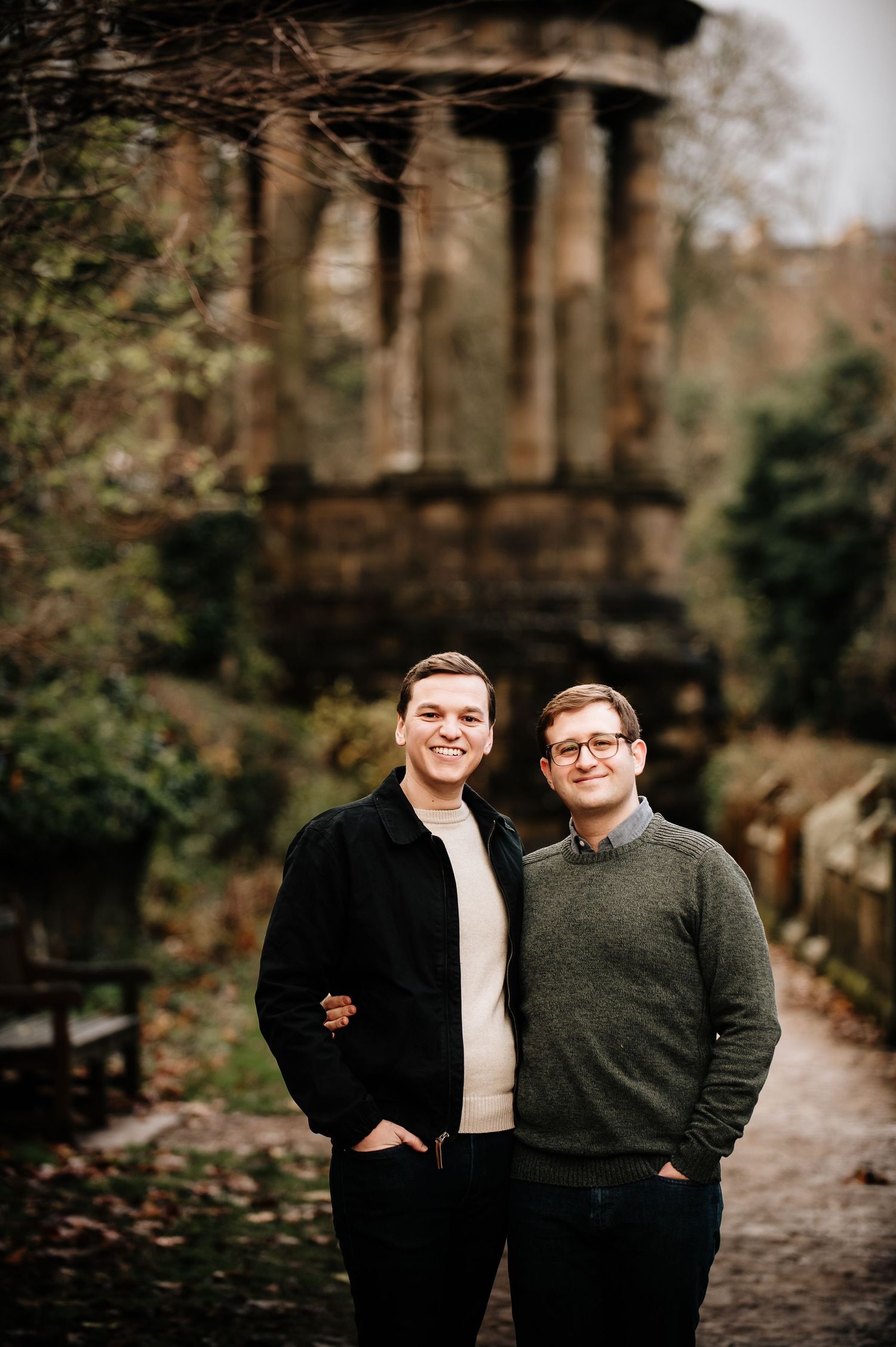 Two people pose together on a path with a classical stone gazebo in the background.