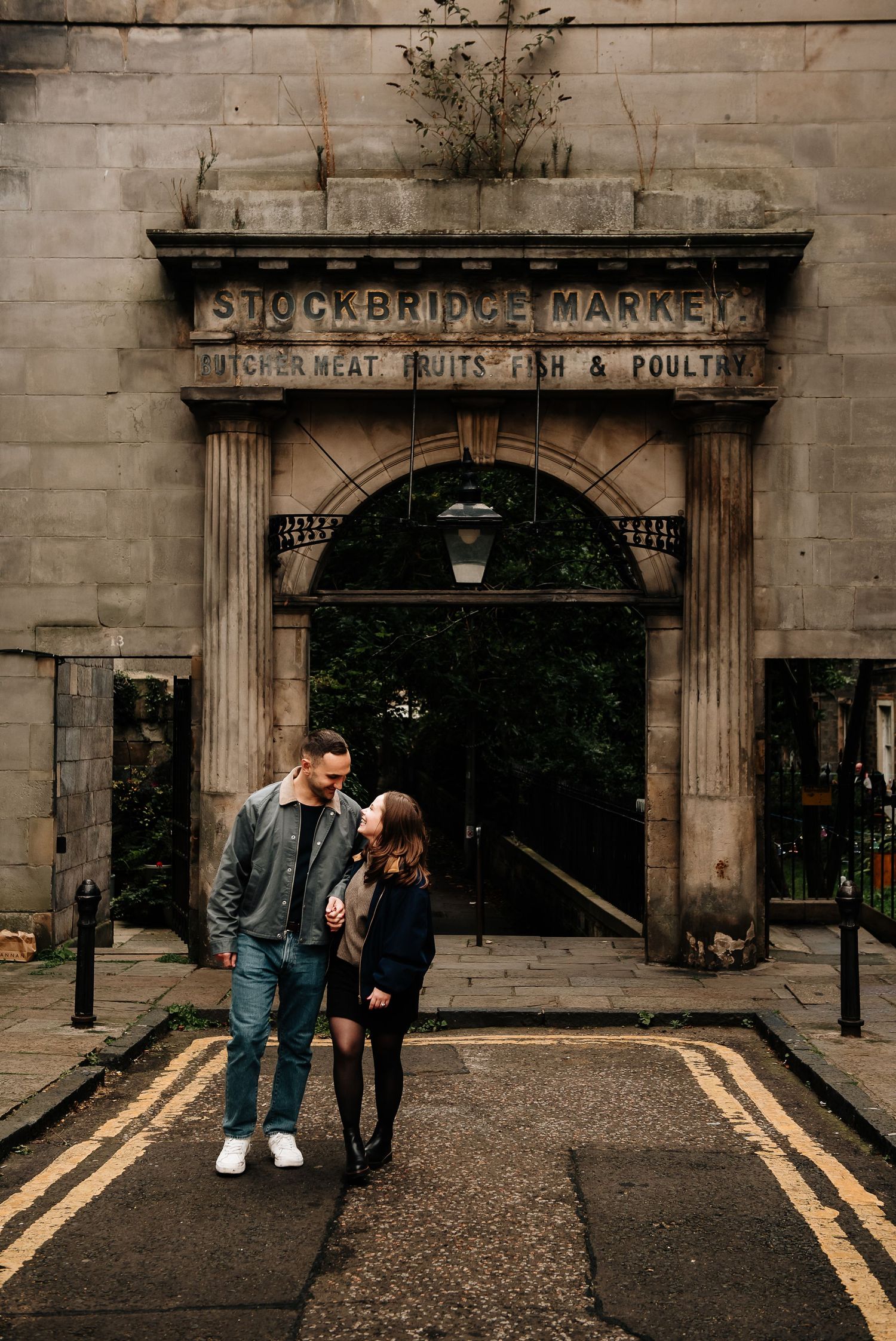 A romantic couple poses in front of the historic Stockbridge Market entrance in Edinburgh.