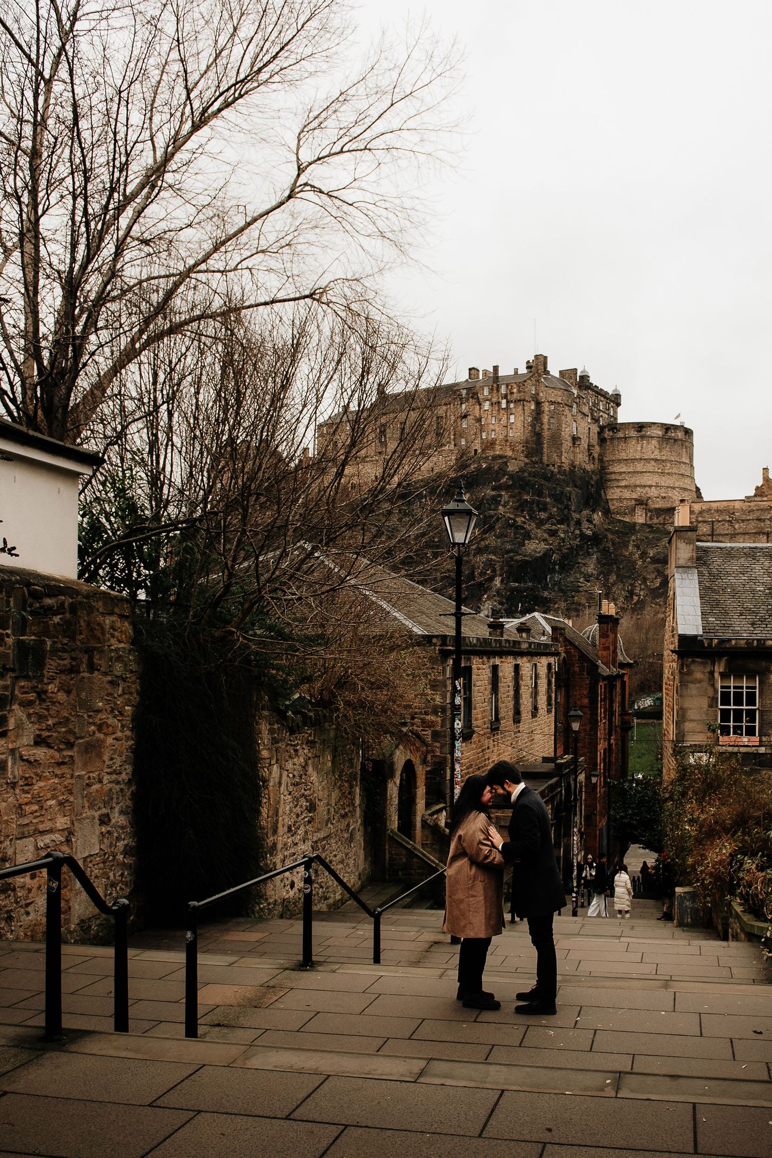 Intimate moment captured on historic Edinburgh street with castle view.
