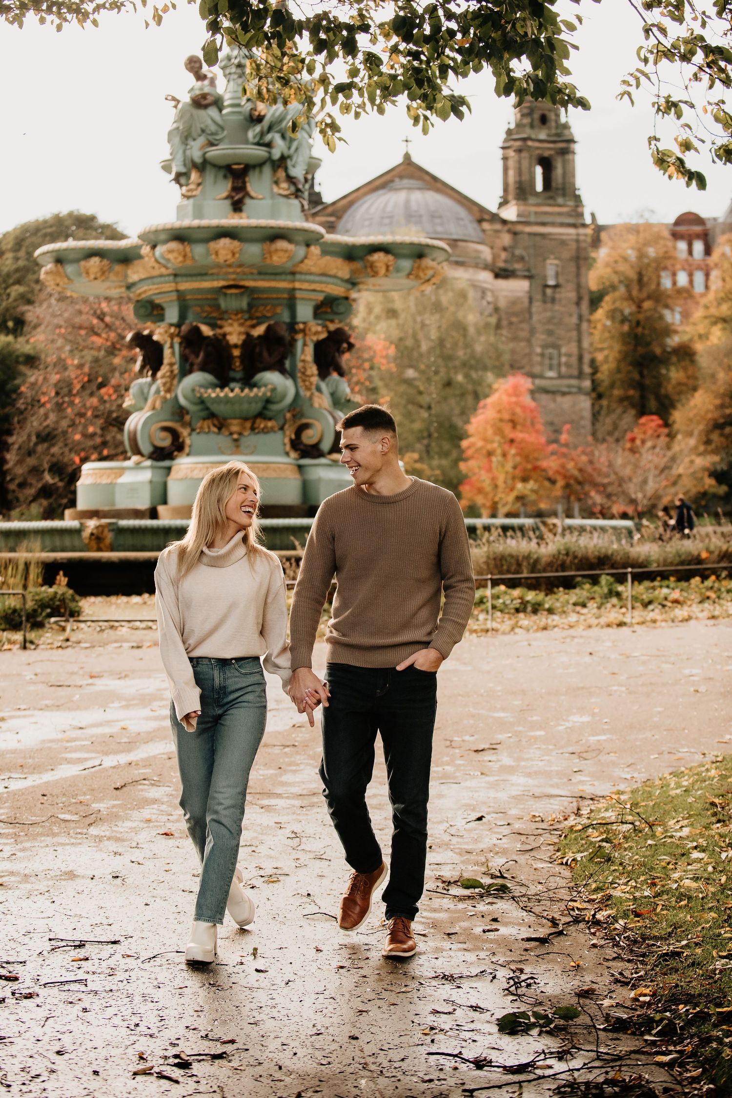 Couple strolls along a scenic path with autumn trees and historic architecture in the background. Edinburgh