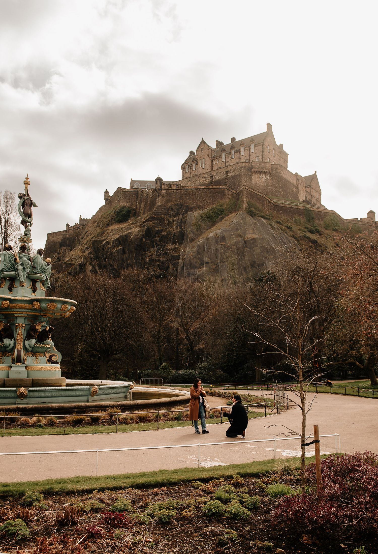 Panoramic view of Edinburgh Castle perched on Castle Rock with the Princes Street Gardens fountain in the foreground.