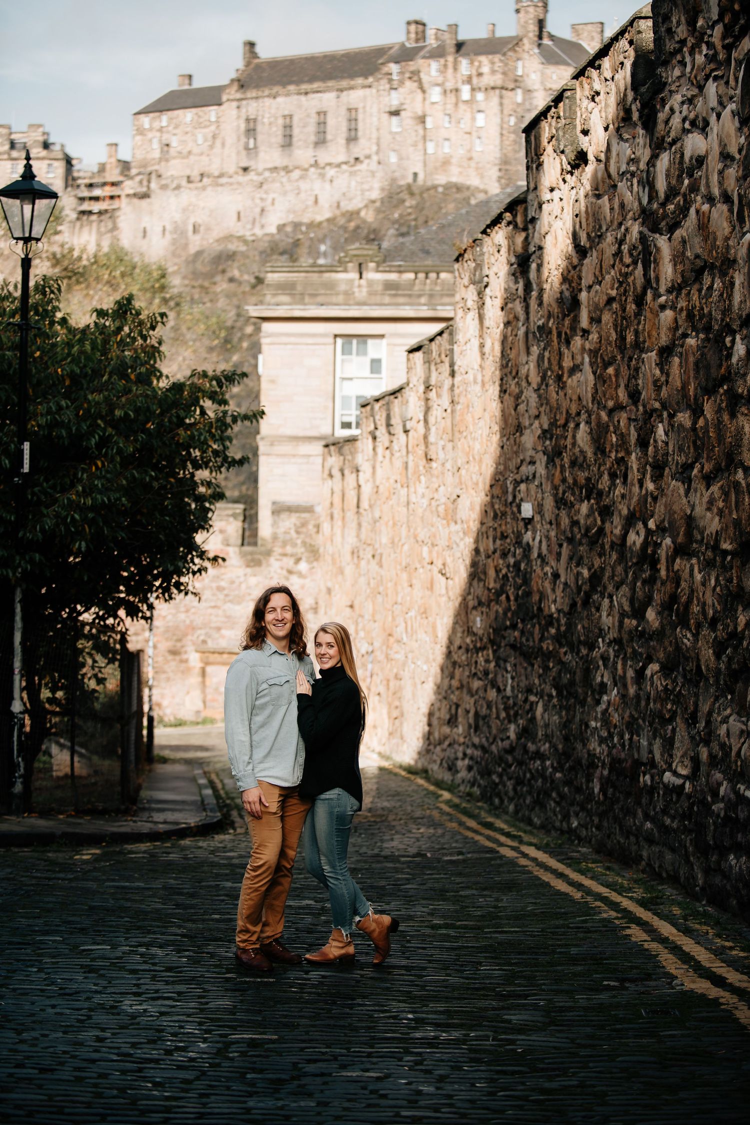 Cobblestone street scene with Edinburgh Castle's walls and architecture in view.