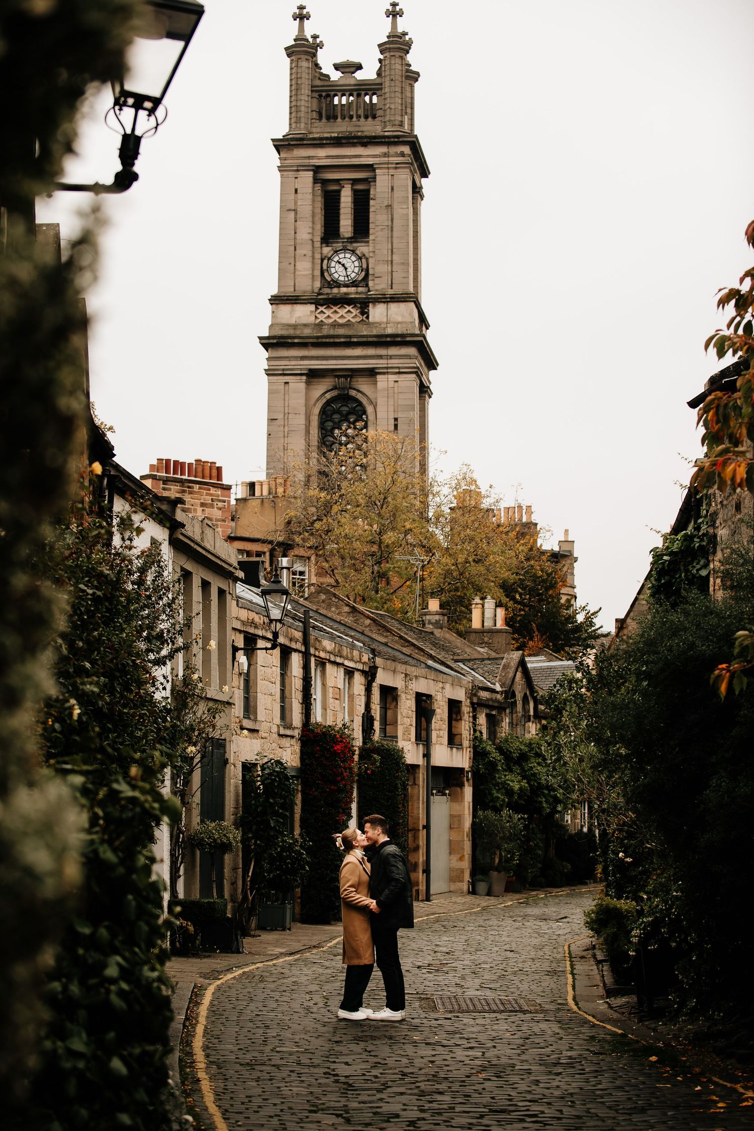 Historic stone buildings line a curved cobblestone street with a tall church spire rising above.