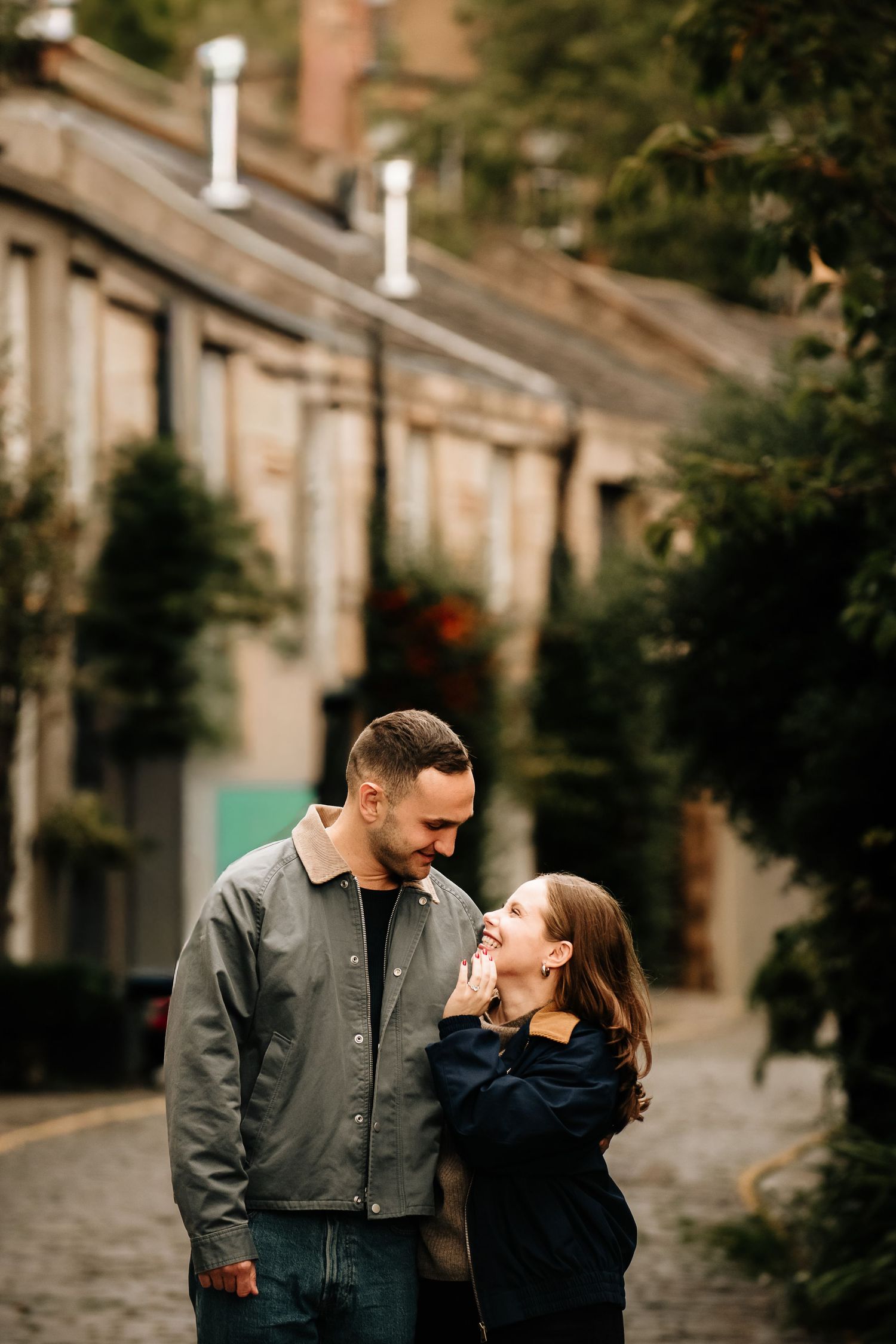A couple embracing on a scenic Edinburgh street with historic stone buildings.