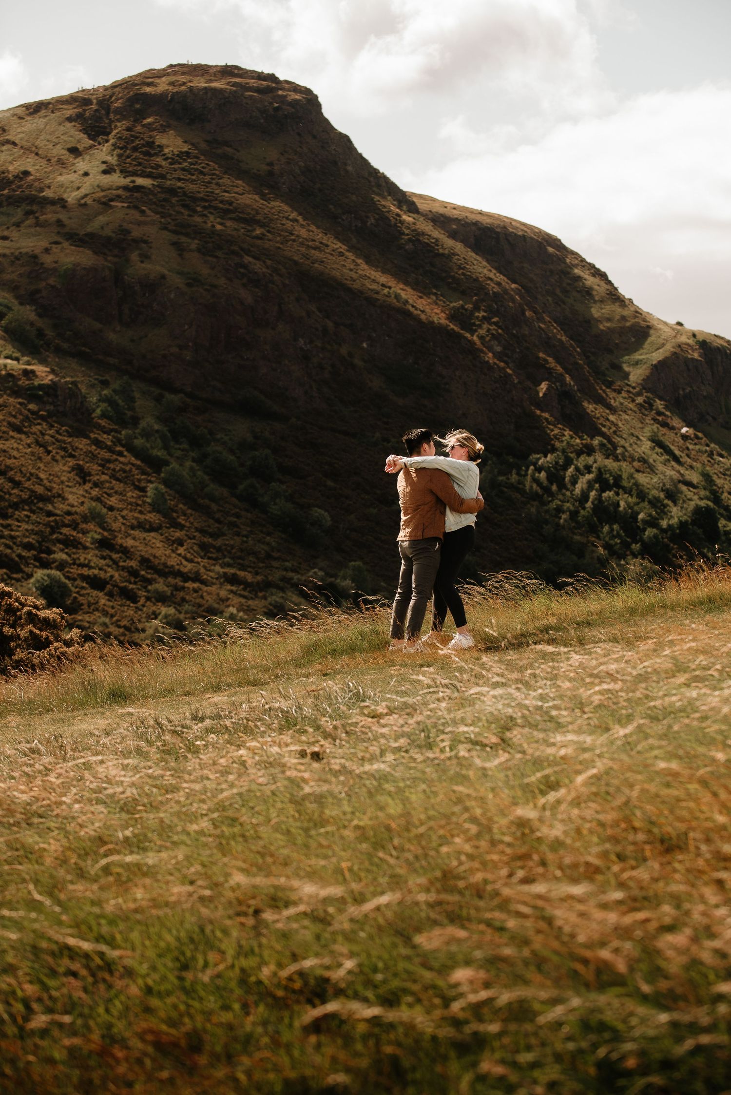 A distant view of people standing on a hillside against a dramatic mountain backdrop.