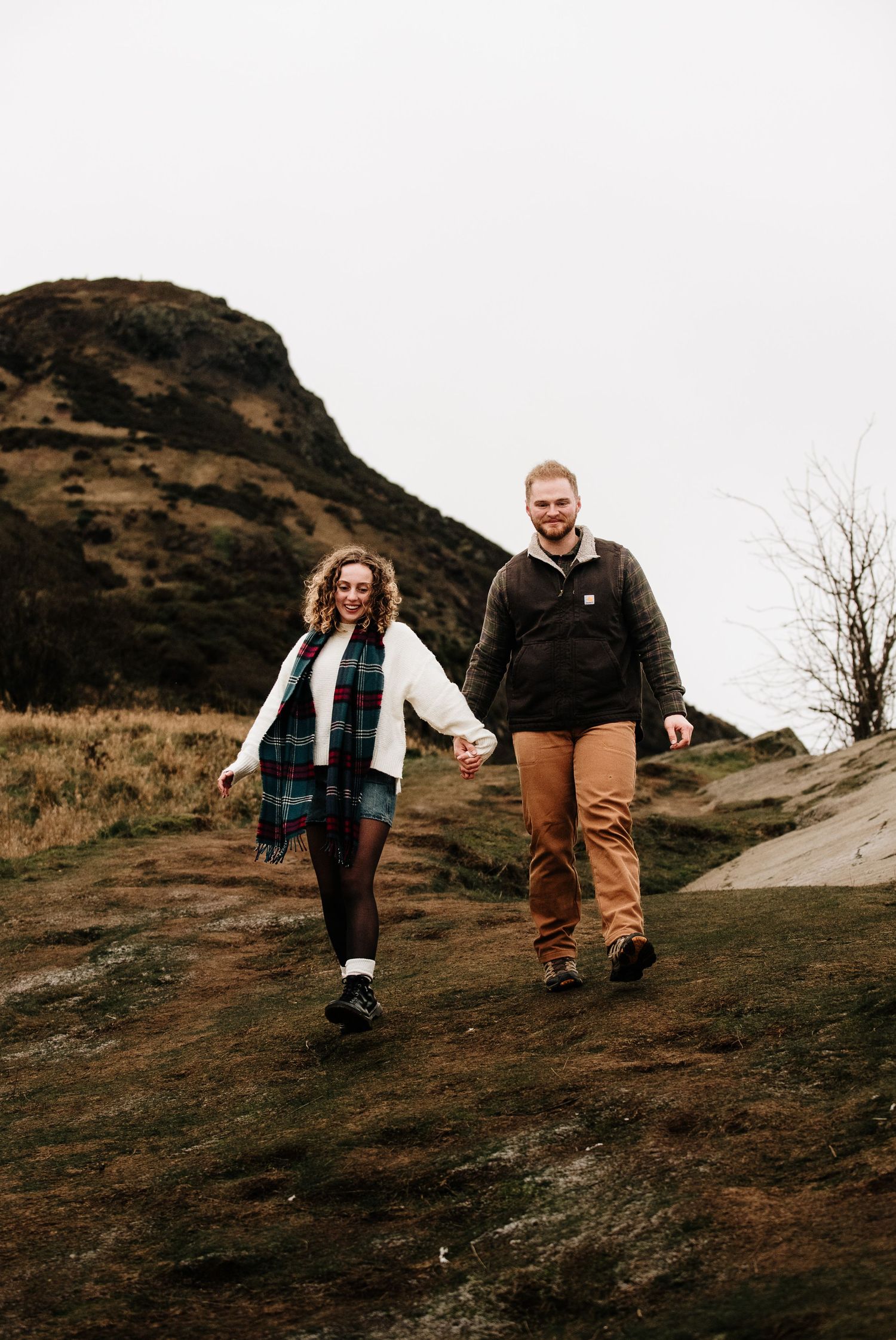 People walking together on a steep hillside trail against a dramatic mountain backdrop.