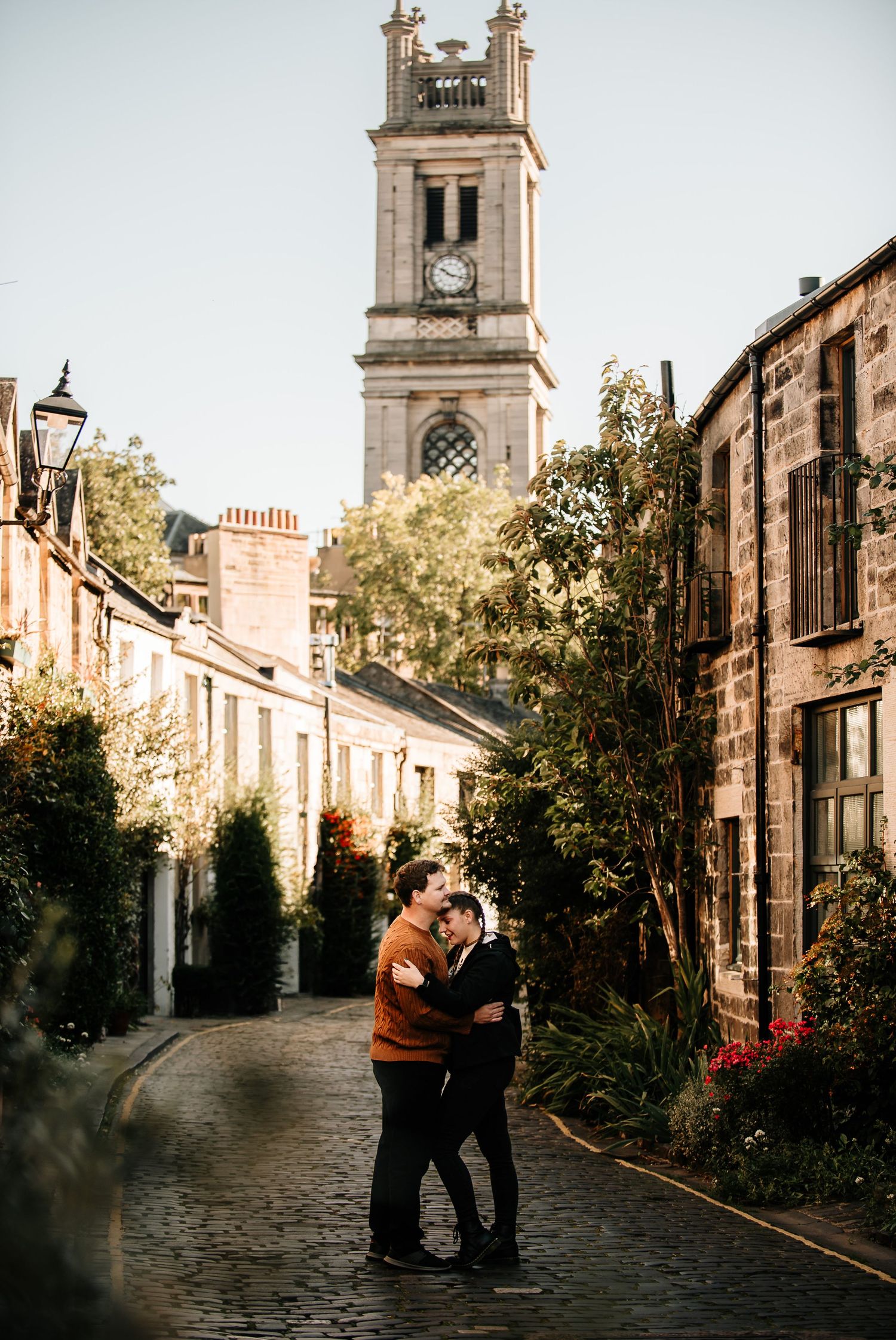 Romantic scene on cobblestone street with historic clock tower in Edinburgh.