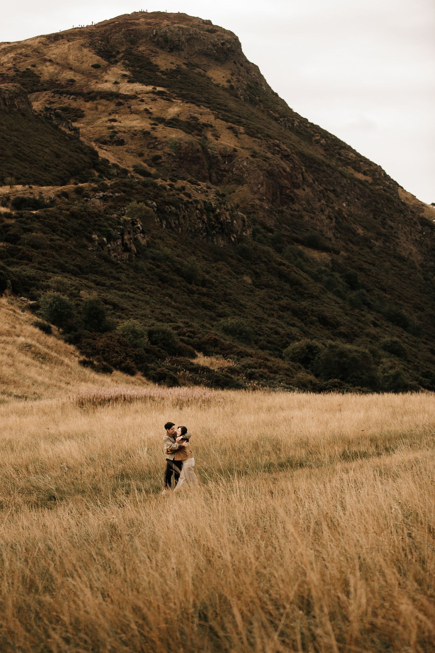 Mountainous landscape with figures walking through tall autumn grass.