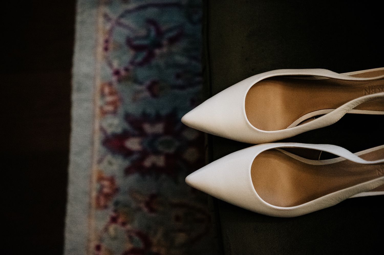 Elegant nude wedding shoes photographed against dark textured background.