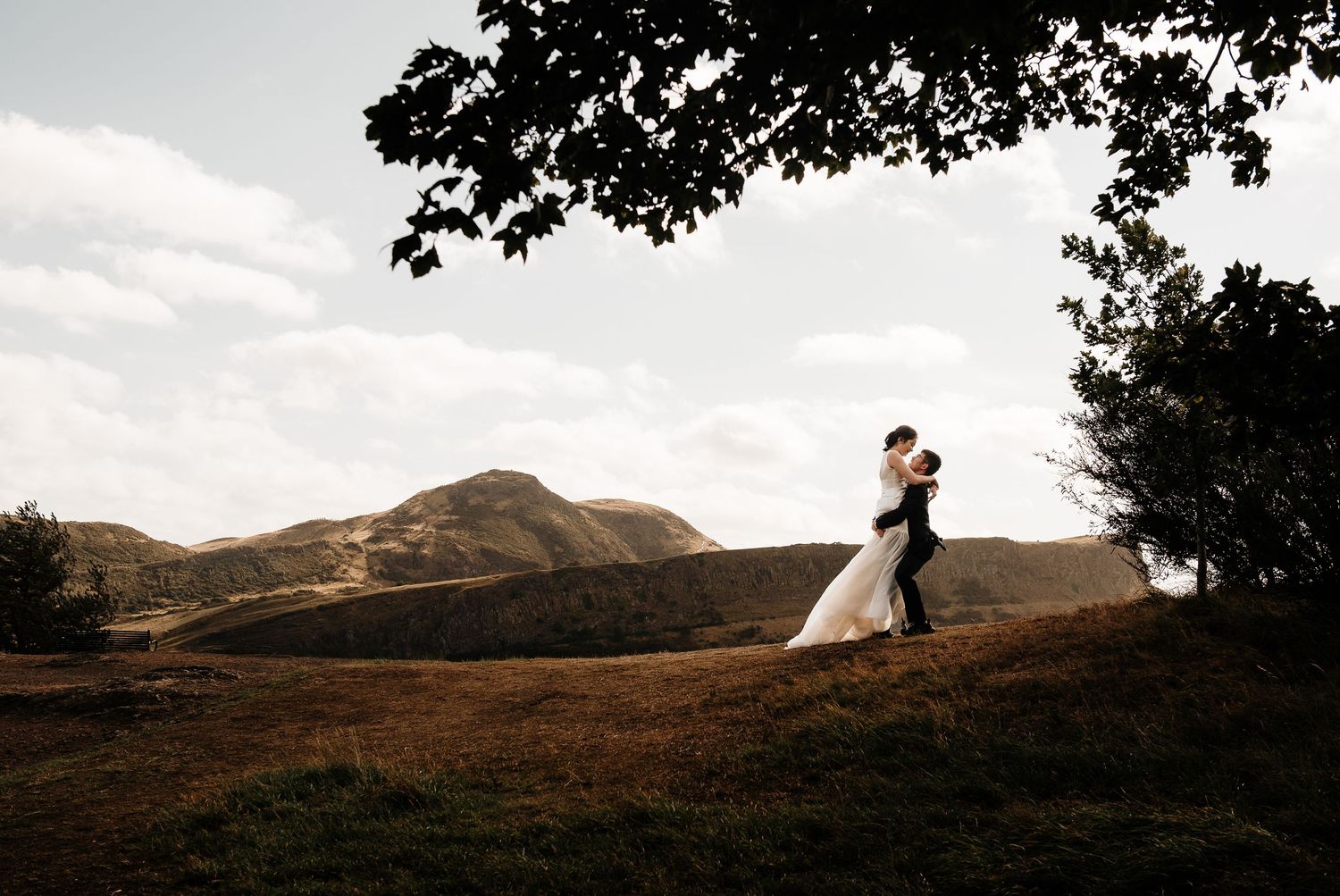 Silhouetted couple on hilltop against dramatic mountain landscape.