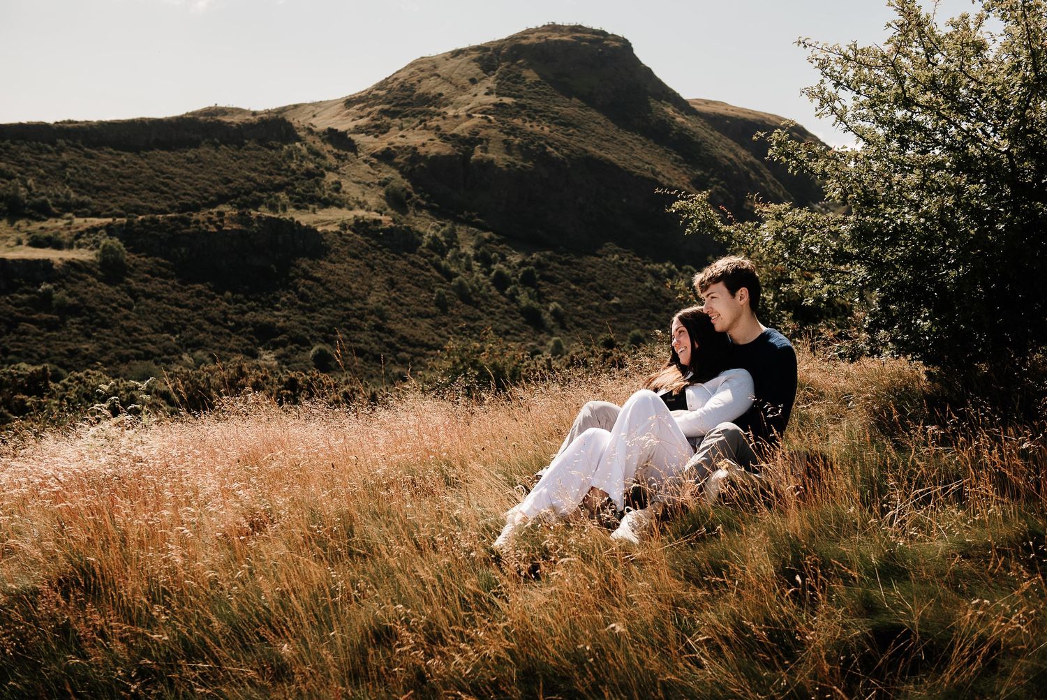 A couple enjoys a romantic moment in tall grass with mountains in the background.