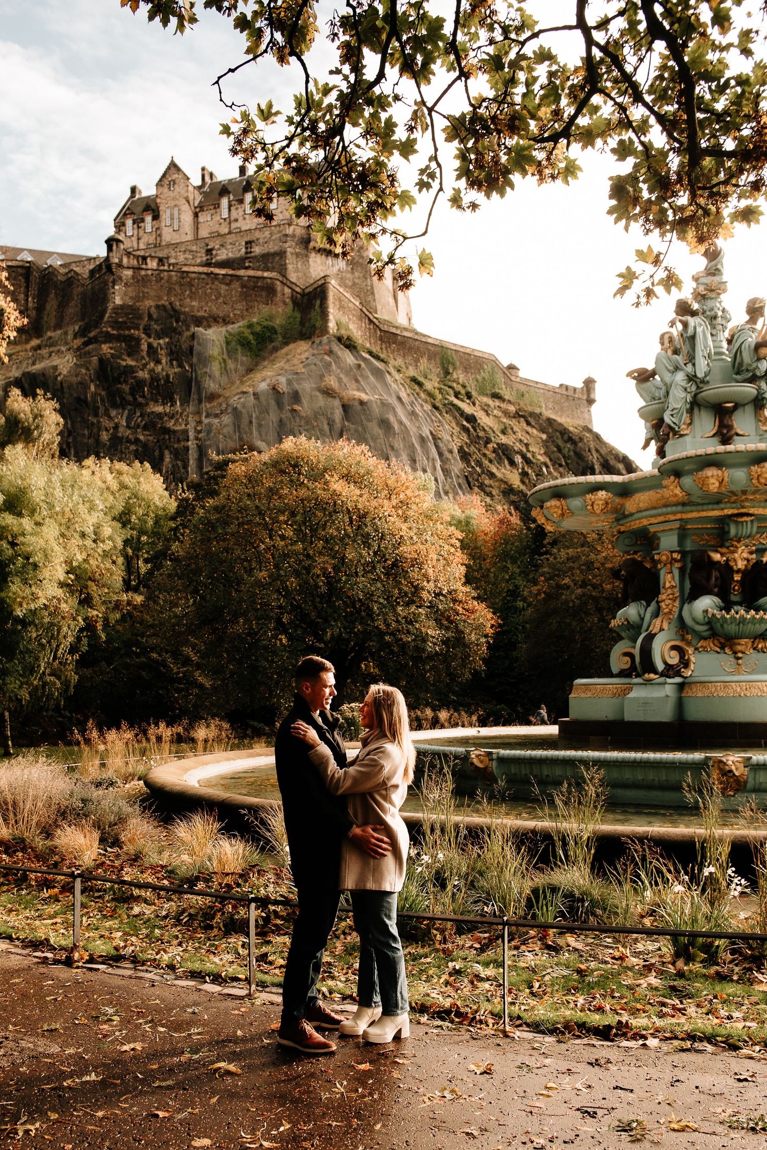 A romantic autumn scene in Edinburgh with couples enjoying the golden hour beneath Edinburgh Castle on a path.