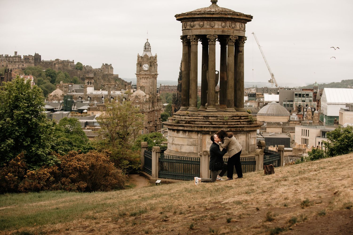 Visitors enjoying view of Edinburgh from Calton Hill with historic monument and cityscape in background.