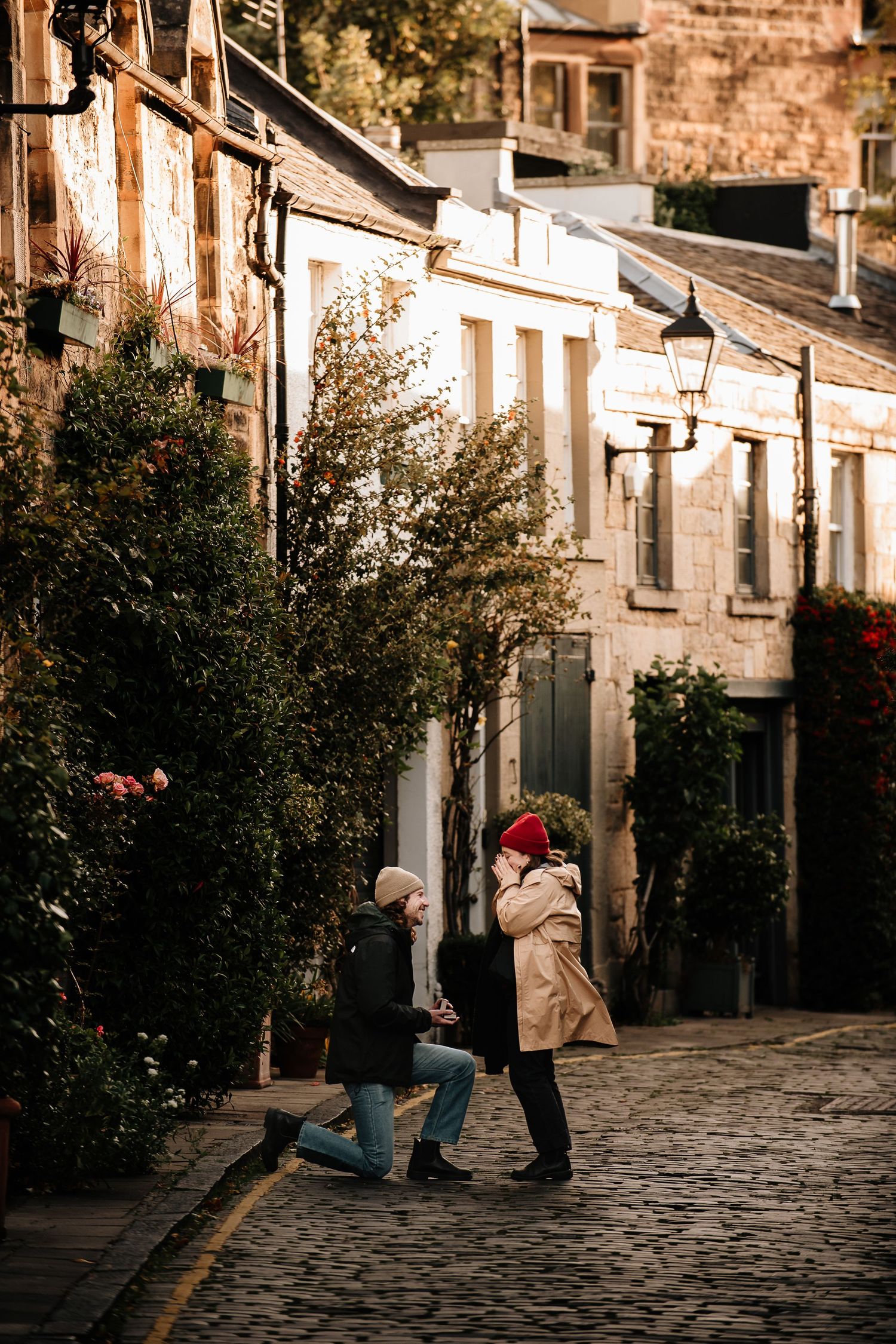 Sunlit cobblestone street with historic stone buildings and autumn foliage.