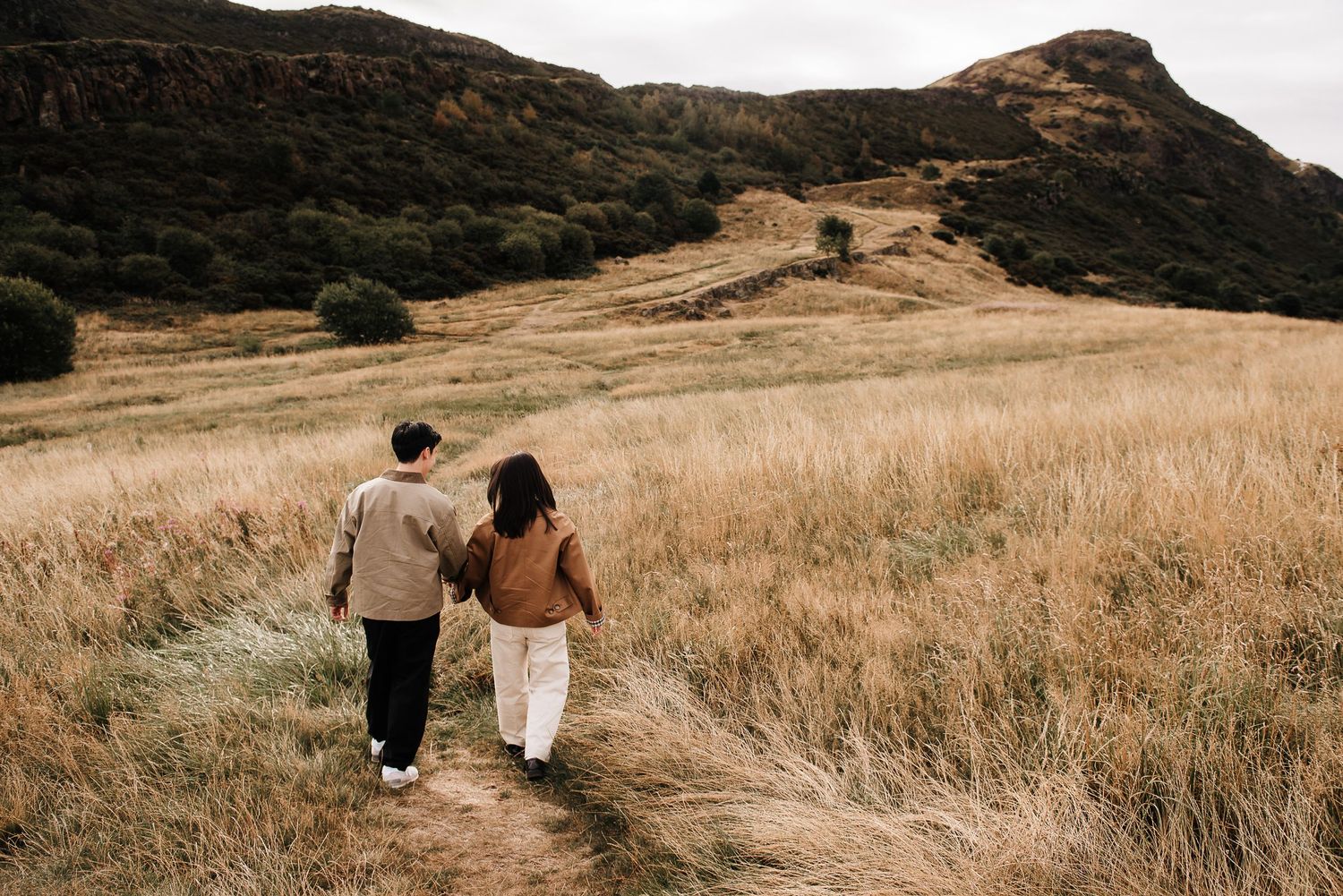 People walking through a scenic mountain meadow with tall golden grass.