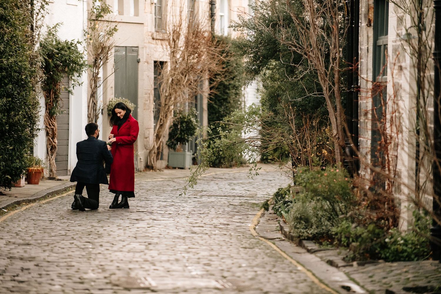 Narrow cobblestone alley lined with historic buildings and winter foliage.