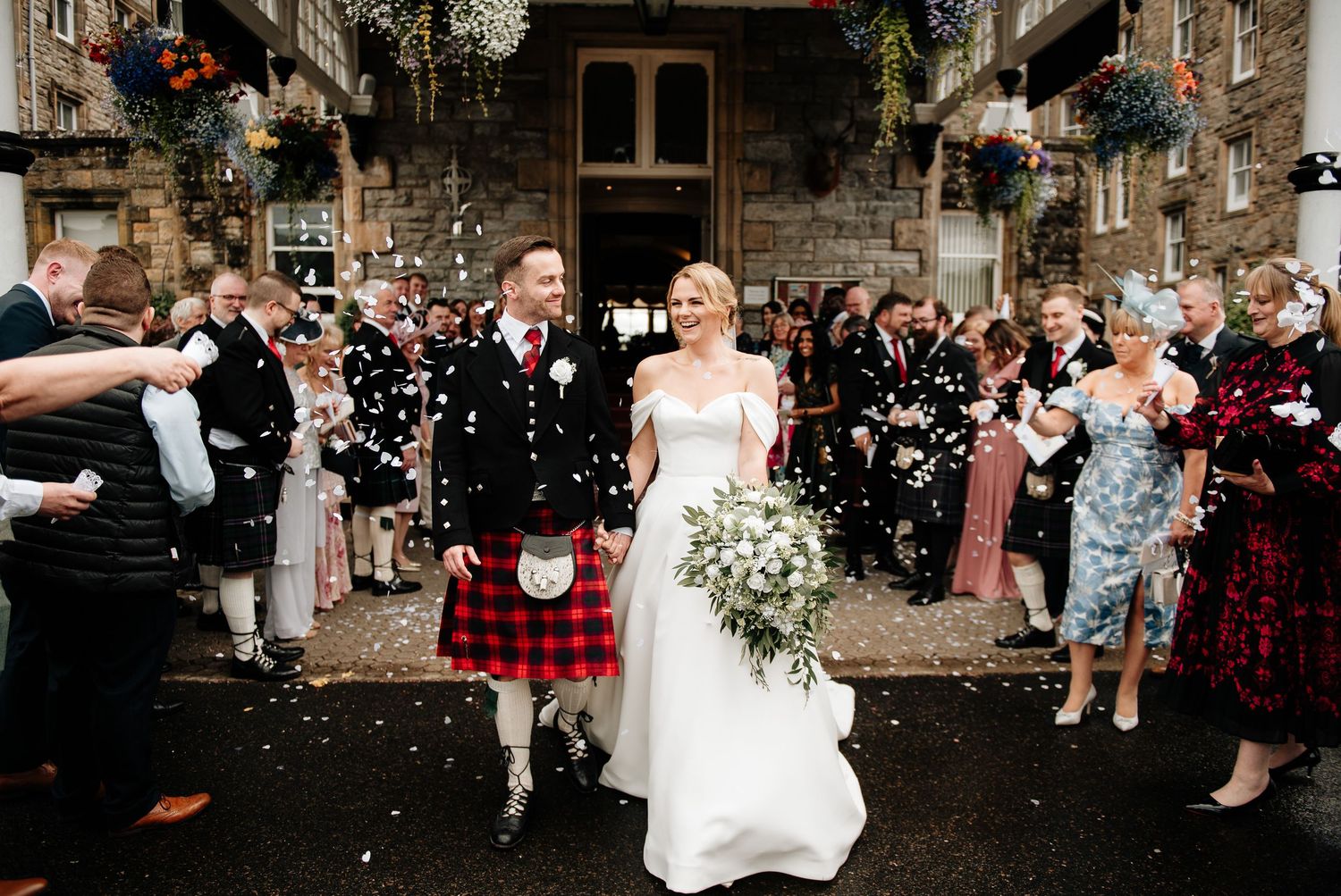 Wedding party and guests celebrating with confetti outside a stone building.