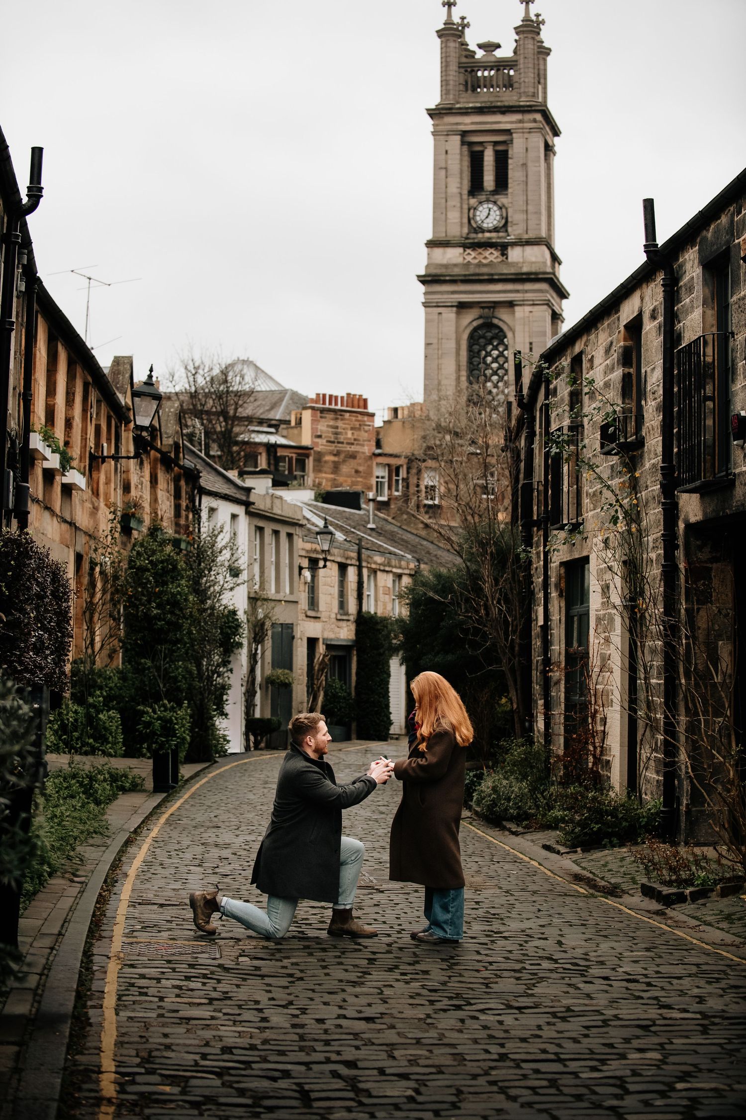A cobblestone street scene in Edinburgh with historic architecture and church spires.