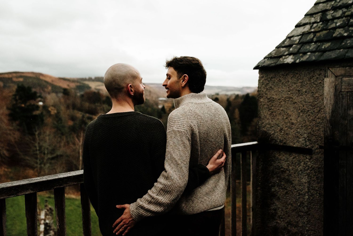 A couple shares an intimate moment on a castle balcony overlooking autumn hills.