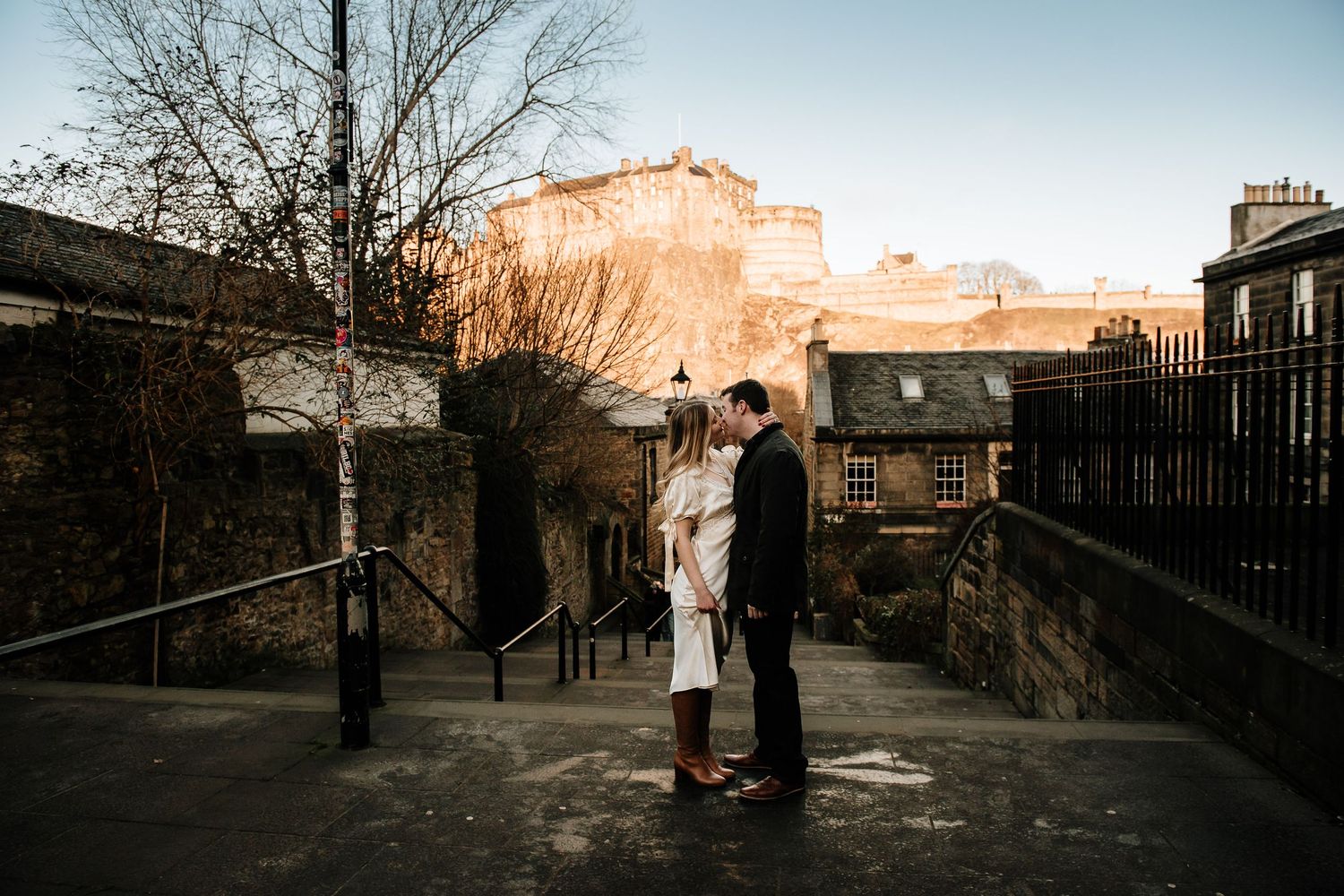 Panoramic view of Edinburgh Castle from a historic stone walkway at dusk.