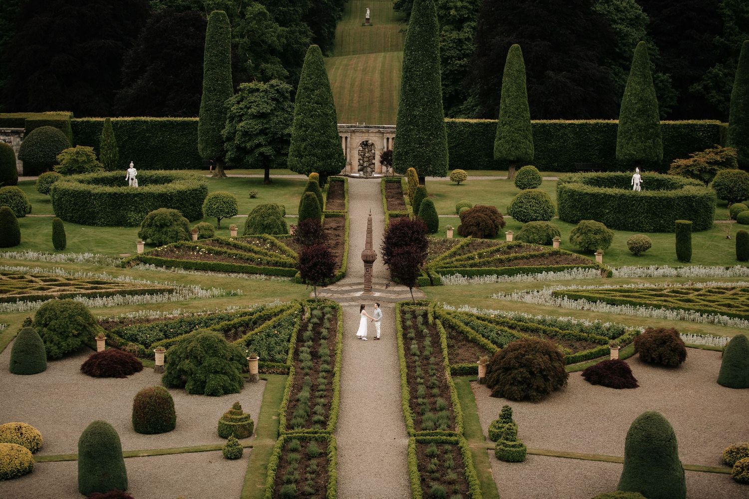 Symmetrical formal garden with manicured hedges and pathways leading to a grand estate.