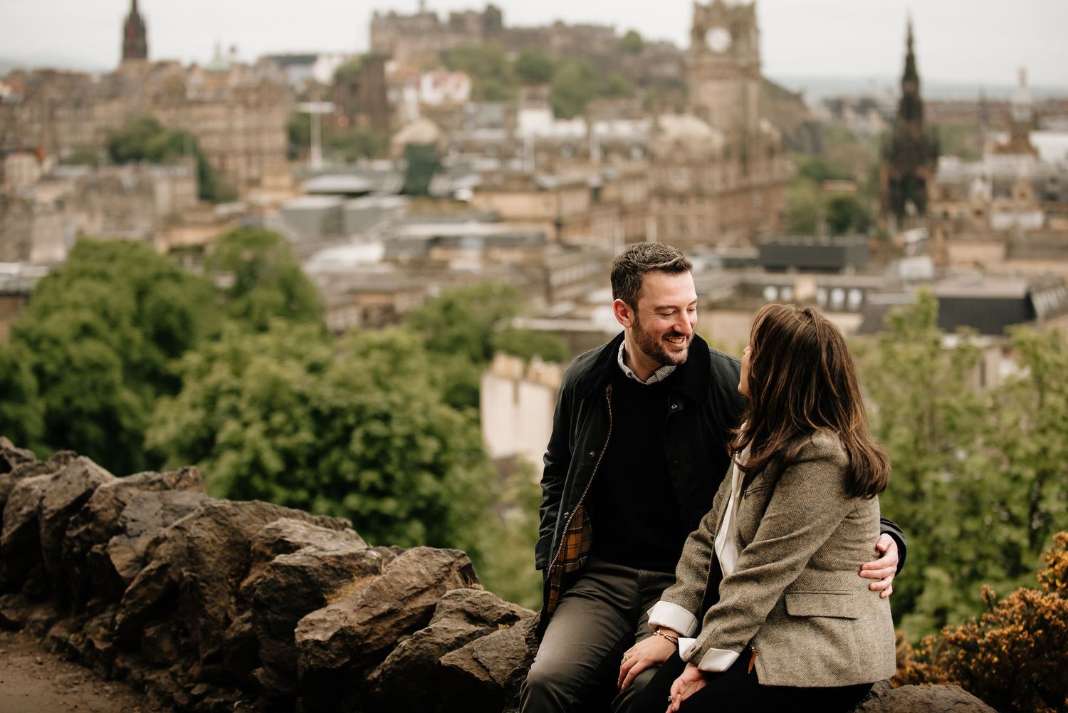 Couple sharing intimate moment on Calton Hill with Edinburgh's historic skyline in background.