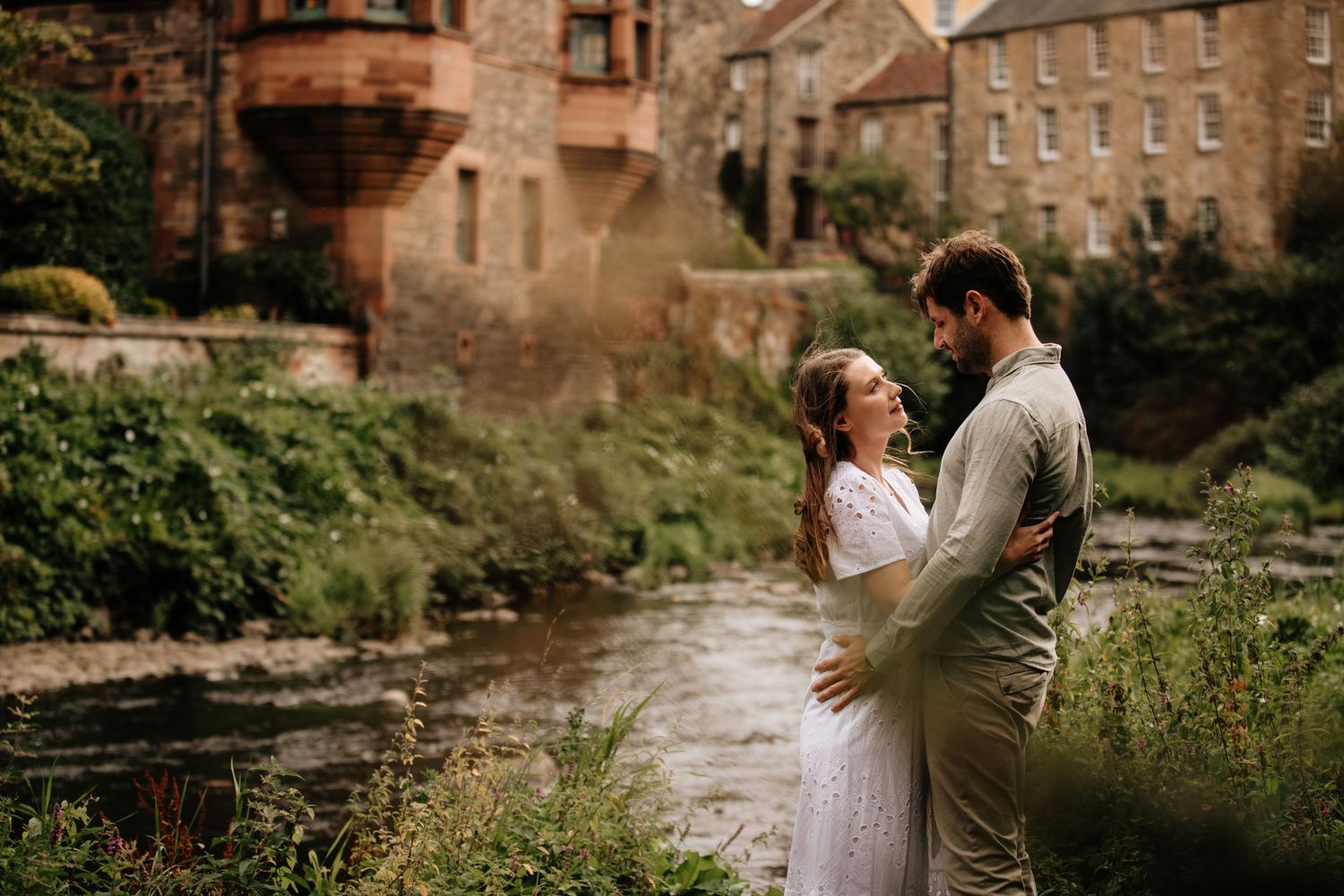 Stone buildings line a picturesque stream in a rustic village setting.