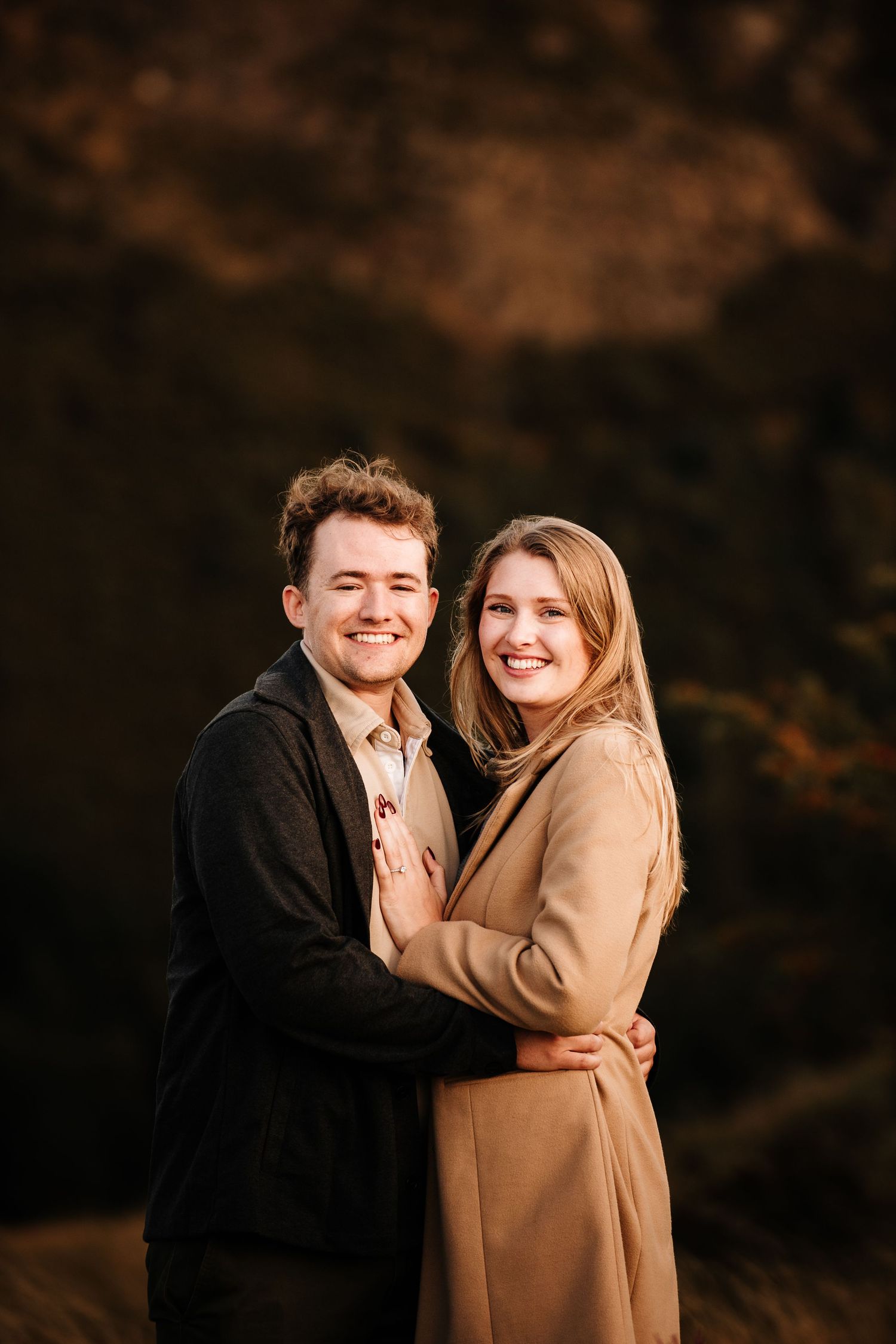 A couple embraces on a scenic hillside during golden hour.