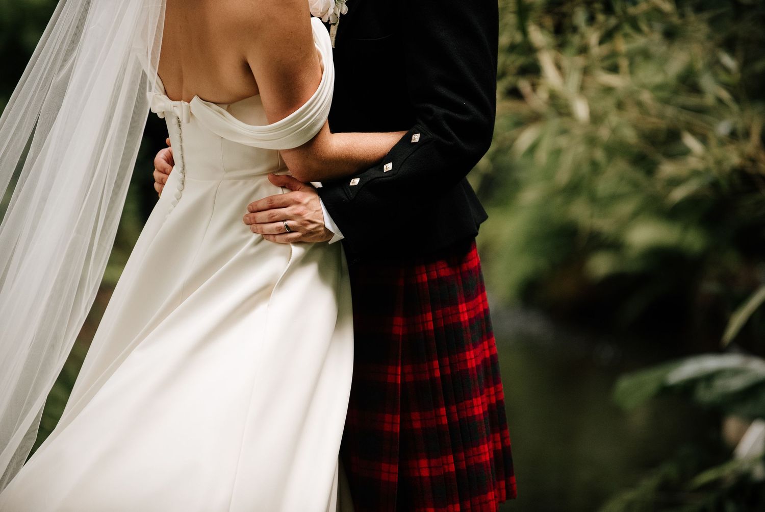 Couple shares romantic moments in a garden setting wearing formal attire and red plaid.