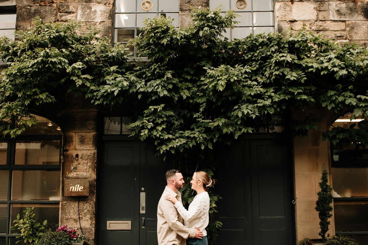 A couple shares a tender moment against ivy-covered walls and dark doorways.