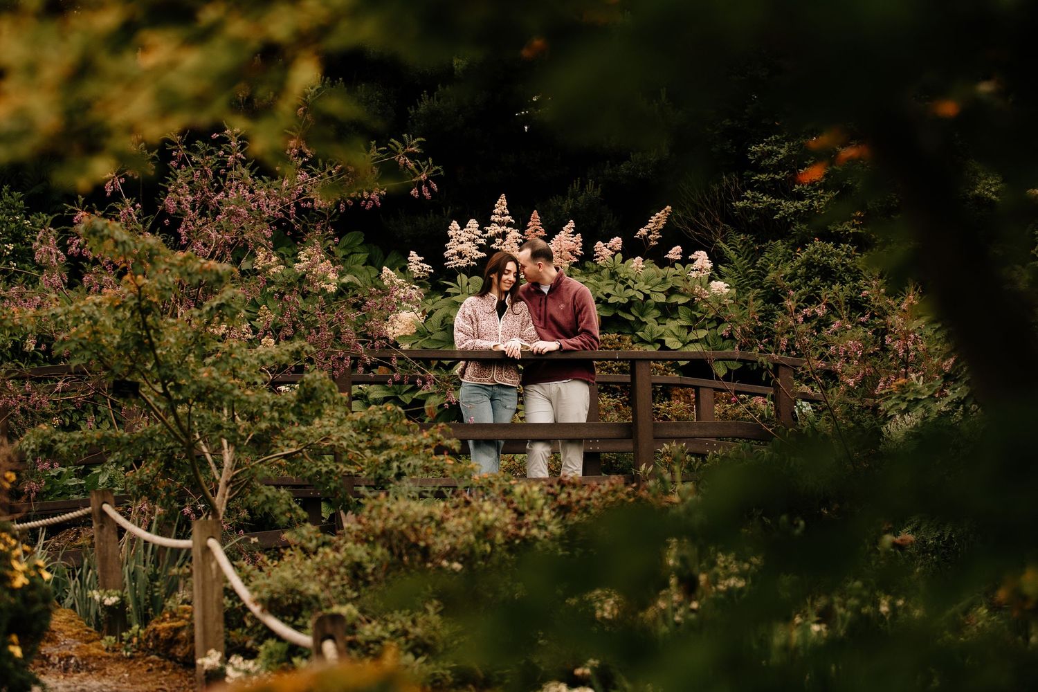 A couple walks through an autumn garden path surrounded by lush foliage.