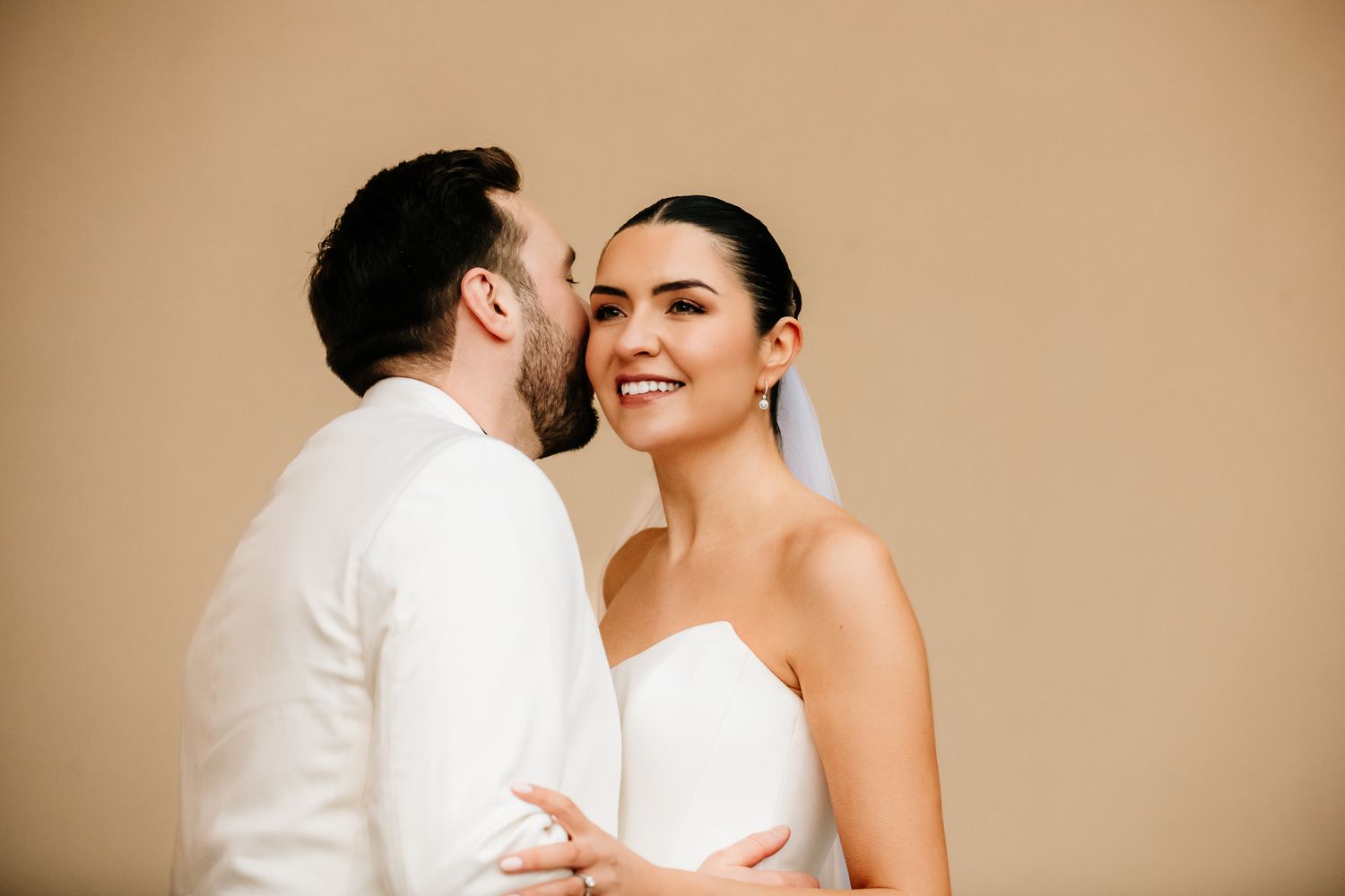 Intimate wedding moment captured against warm neutral background.