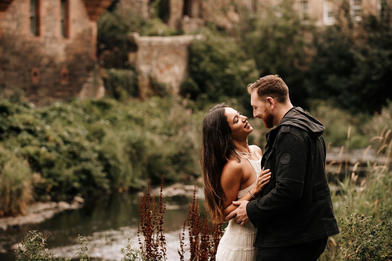 A couple shares an intimate moment by a tranquil riverside setting.