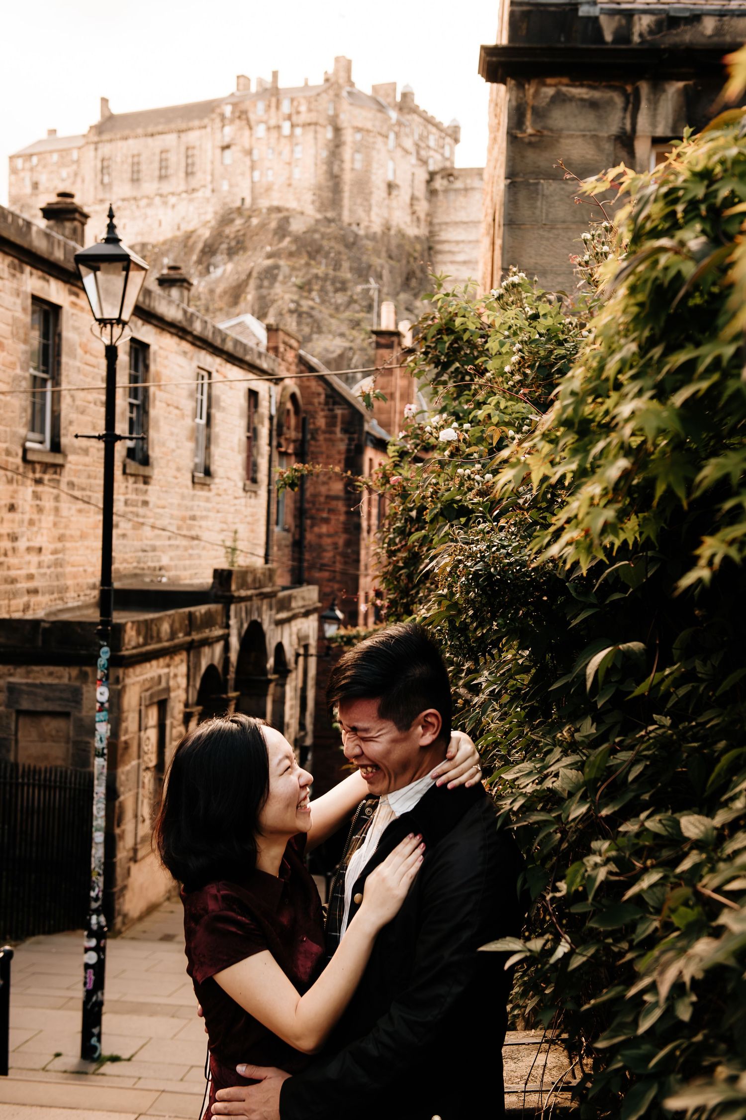 Couple embracing and laughing in Edinburgh's Old Town with the historic castle on the rock in the background.