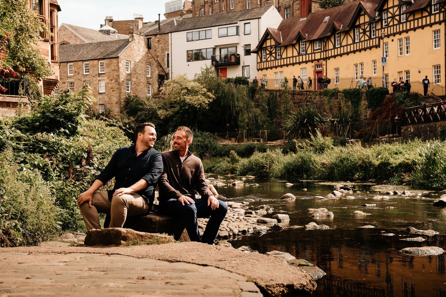 Couple enjoying a peaceful moment by a scenic river with historic buildings in the background.
