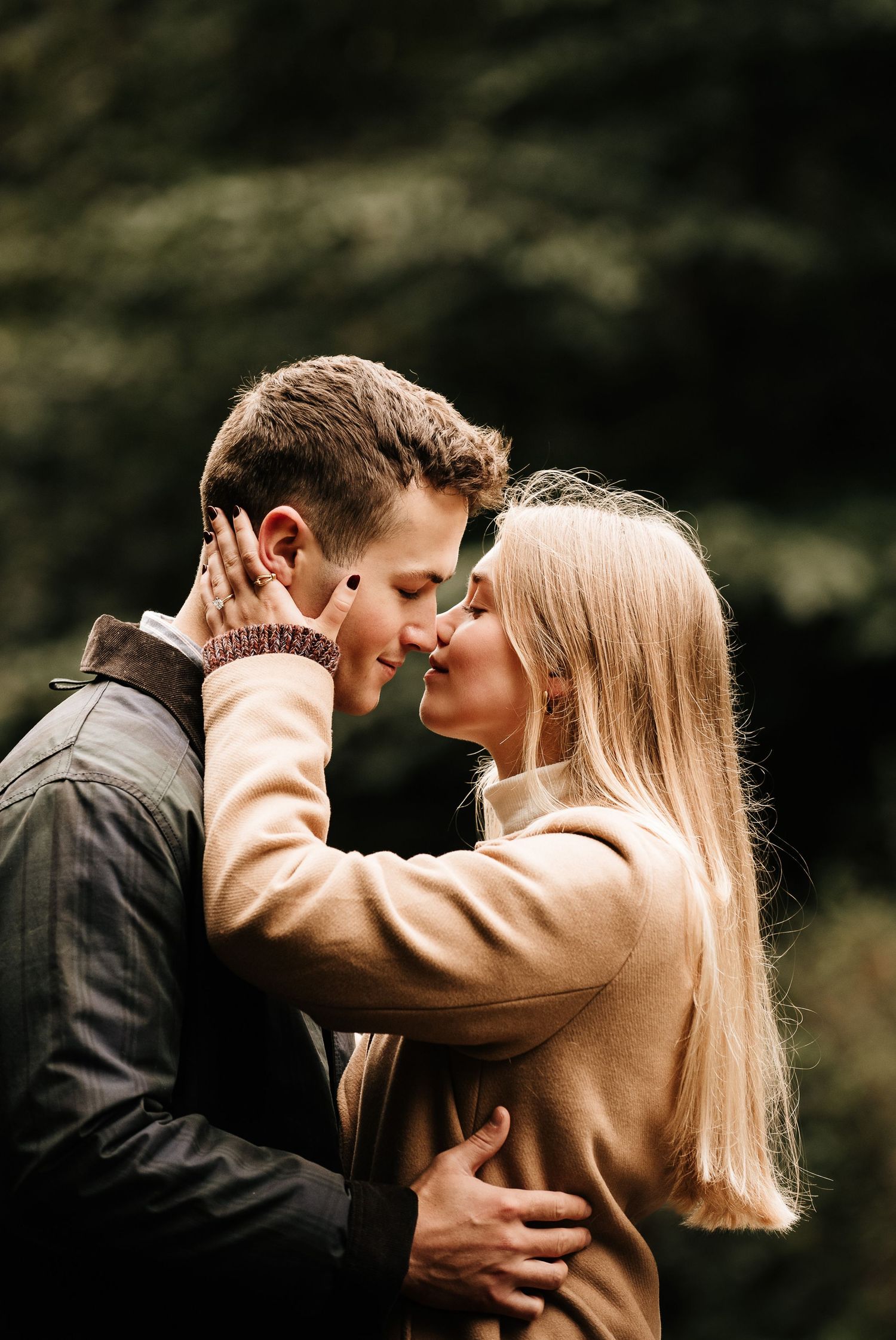 Intimate close-up of a romantic couple in warm autumn clothing against a dark forest background.